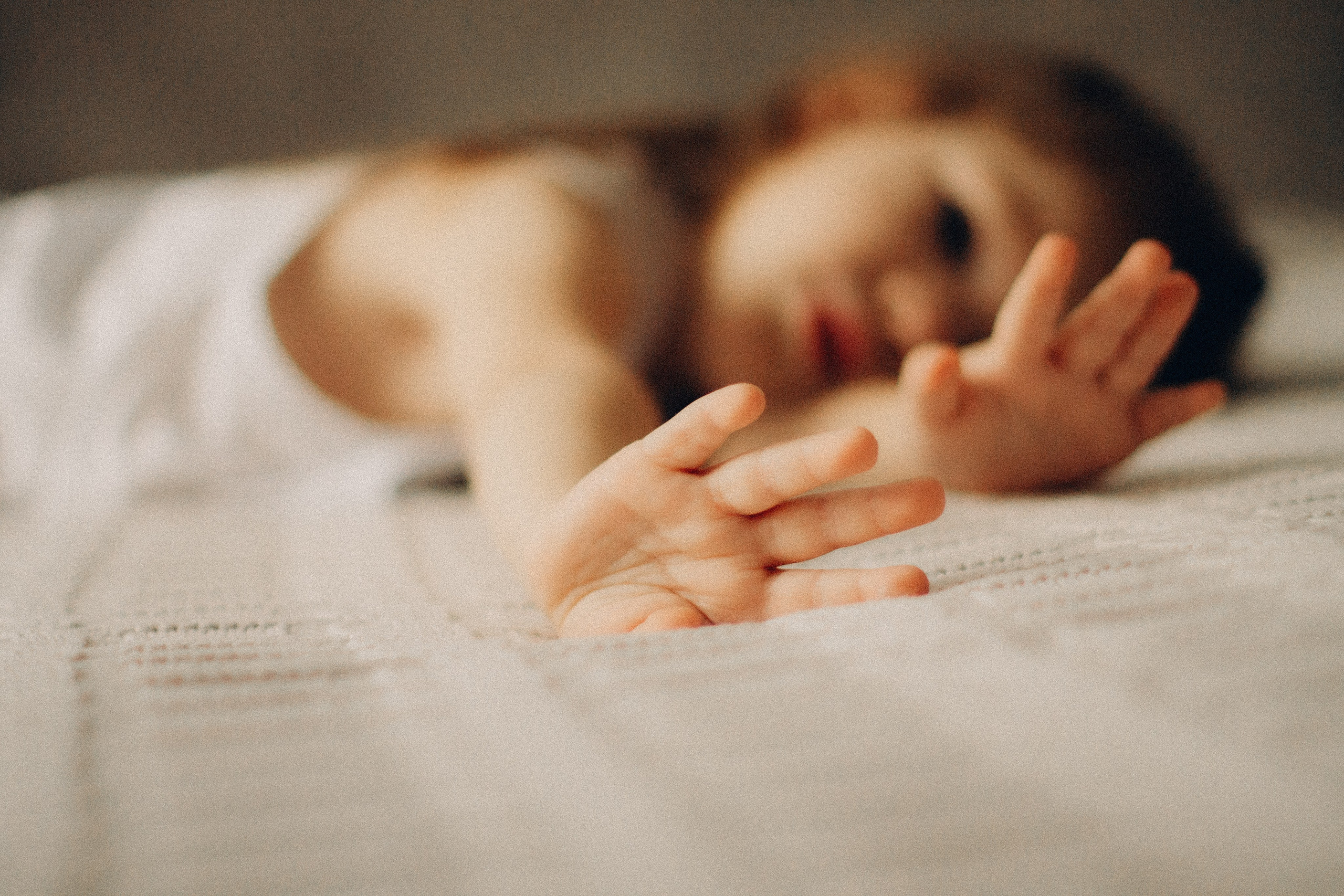 фотография девочки двух лет на кровати, девочка на кровати рассматривает свои ручки, руки на переднем плане