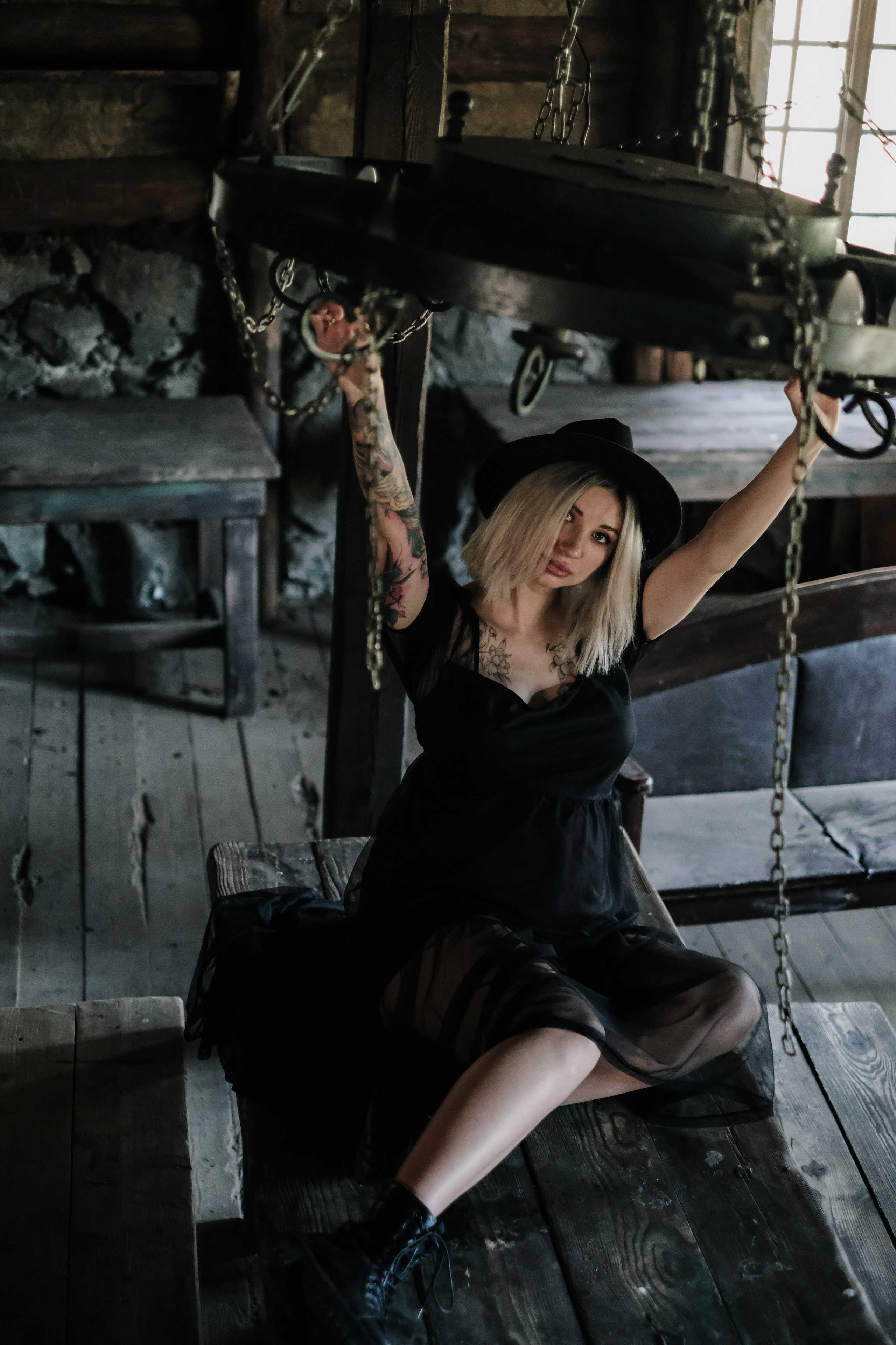 Беременная девушка в черном платье и шляпе с цепями в старом заброшенном доме