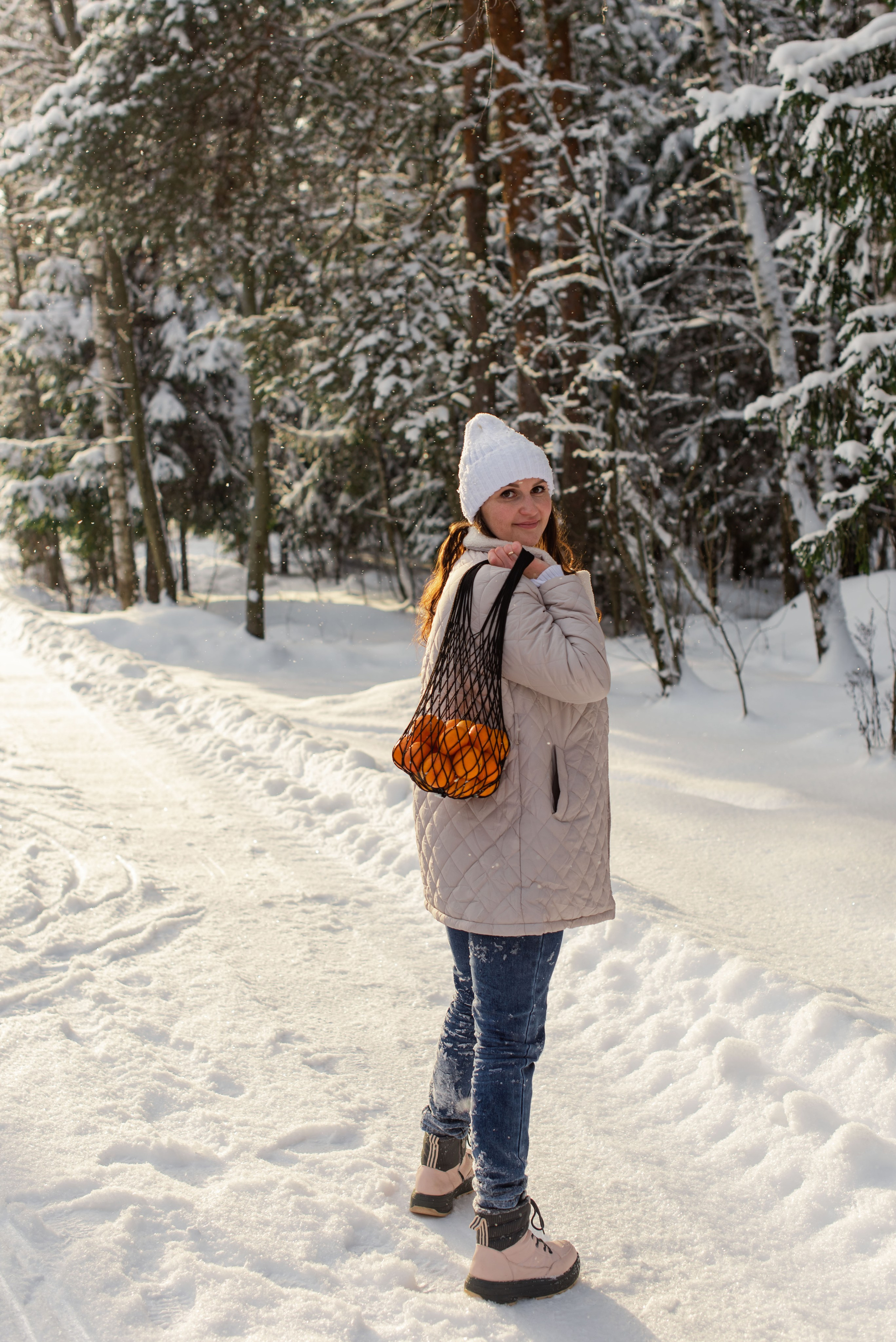 Зимняя сцена: девушка держит сетку с цитрусовыми, вокруг — лесная местность.