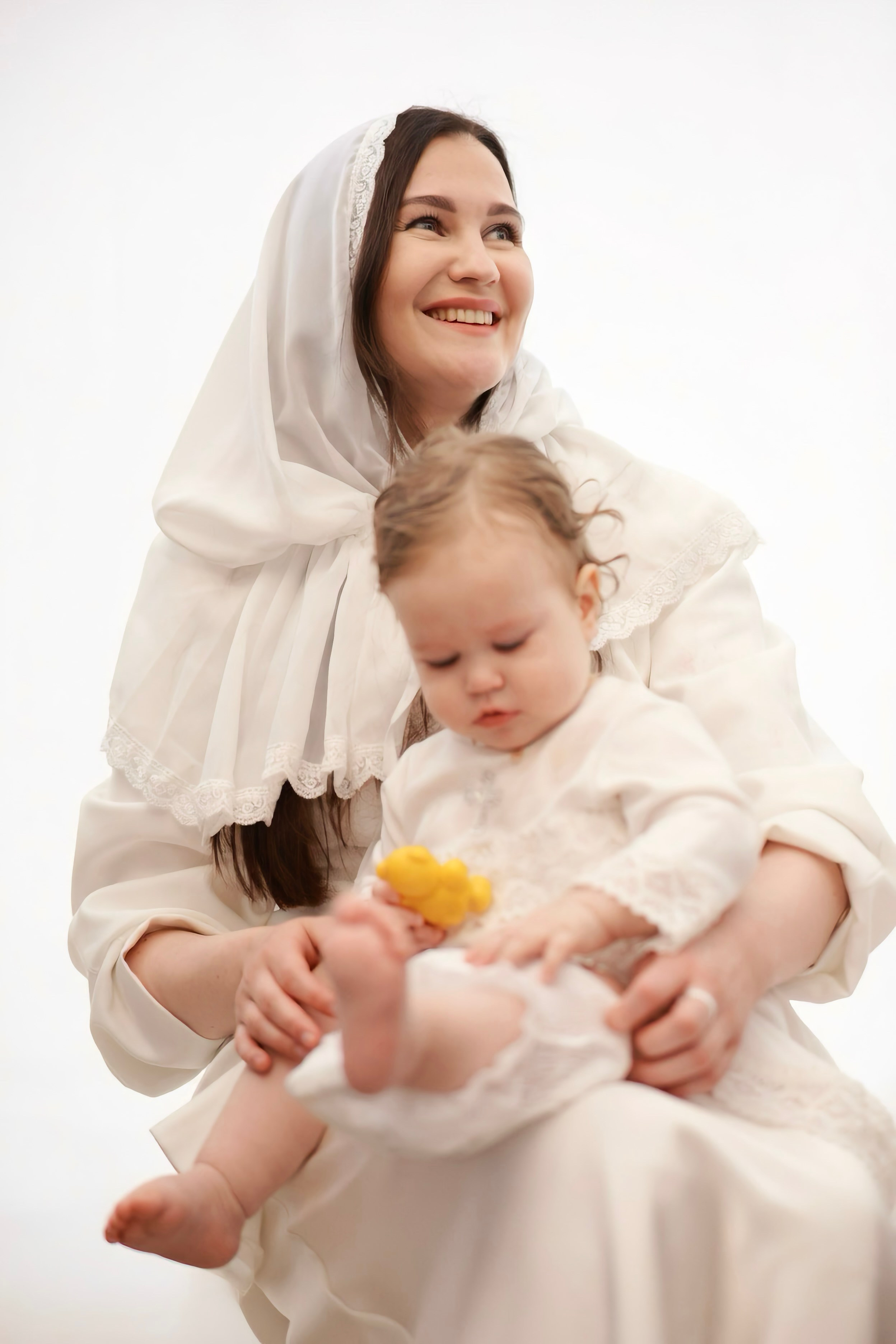 Крестная мать в белом плате держит младенца в крестильной рубашке, светлый фон — Екатеринбург, Илья Антропов