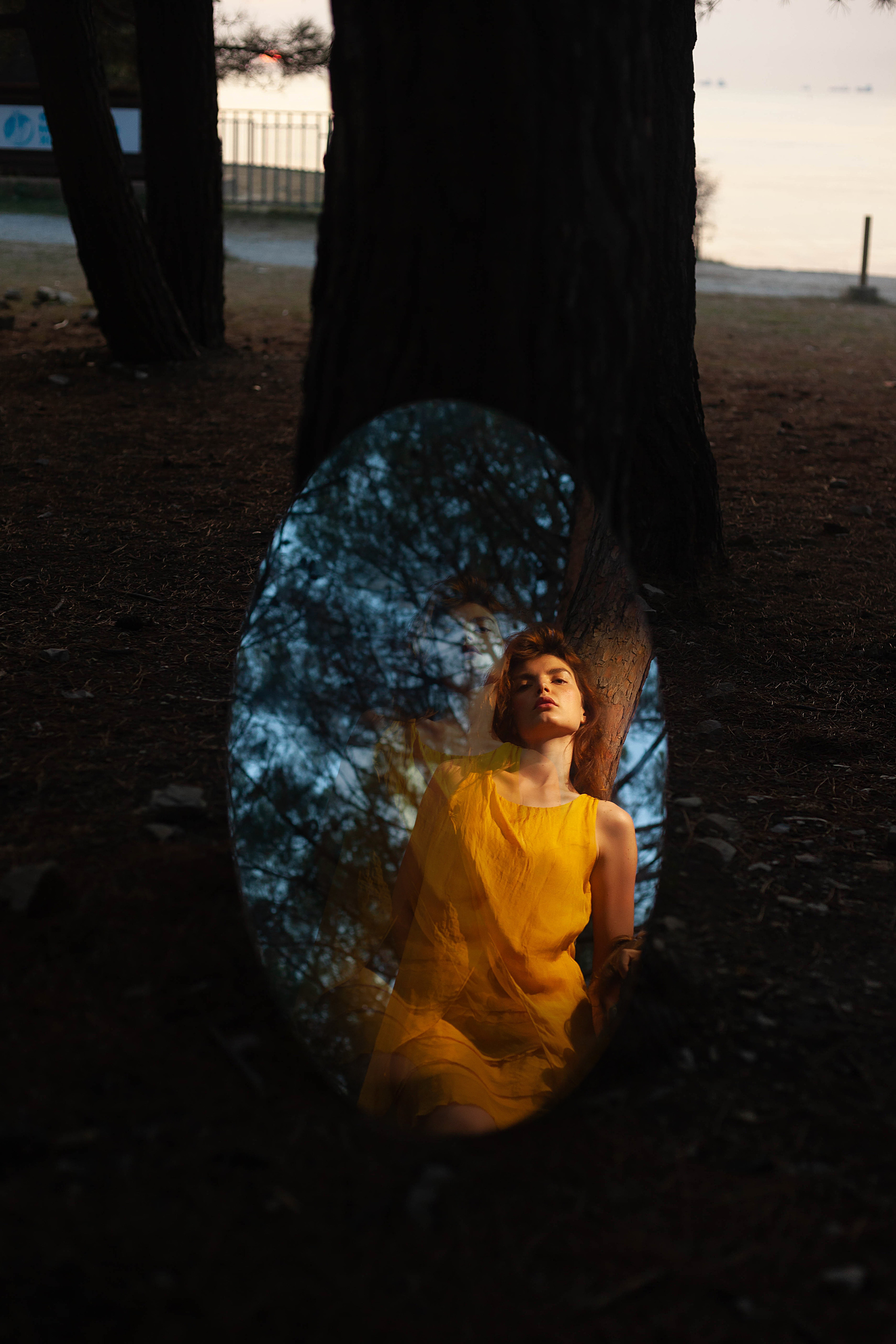 на дерево опирается зеркало отражающее девушку в желтом платье