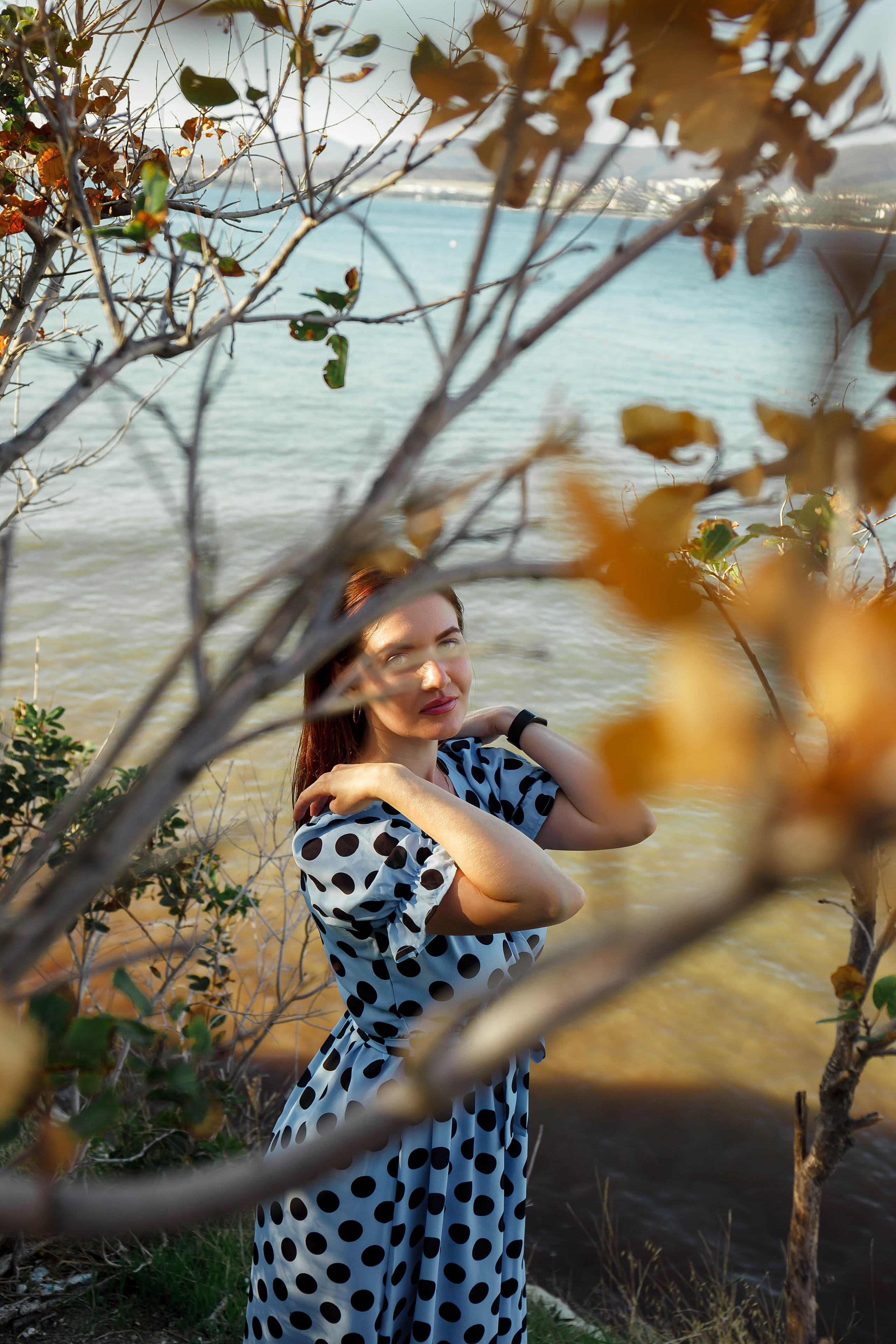 девушка в голубом платье в горошек стоит у красивых деревьев