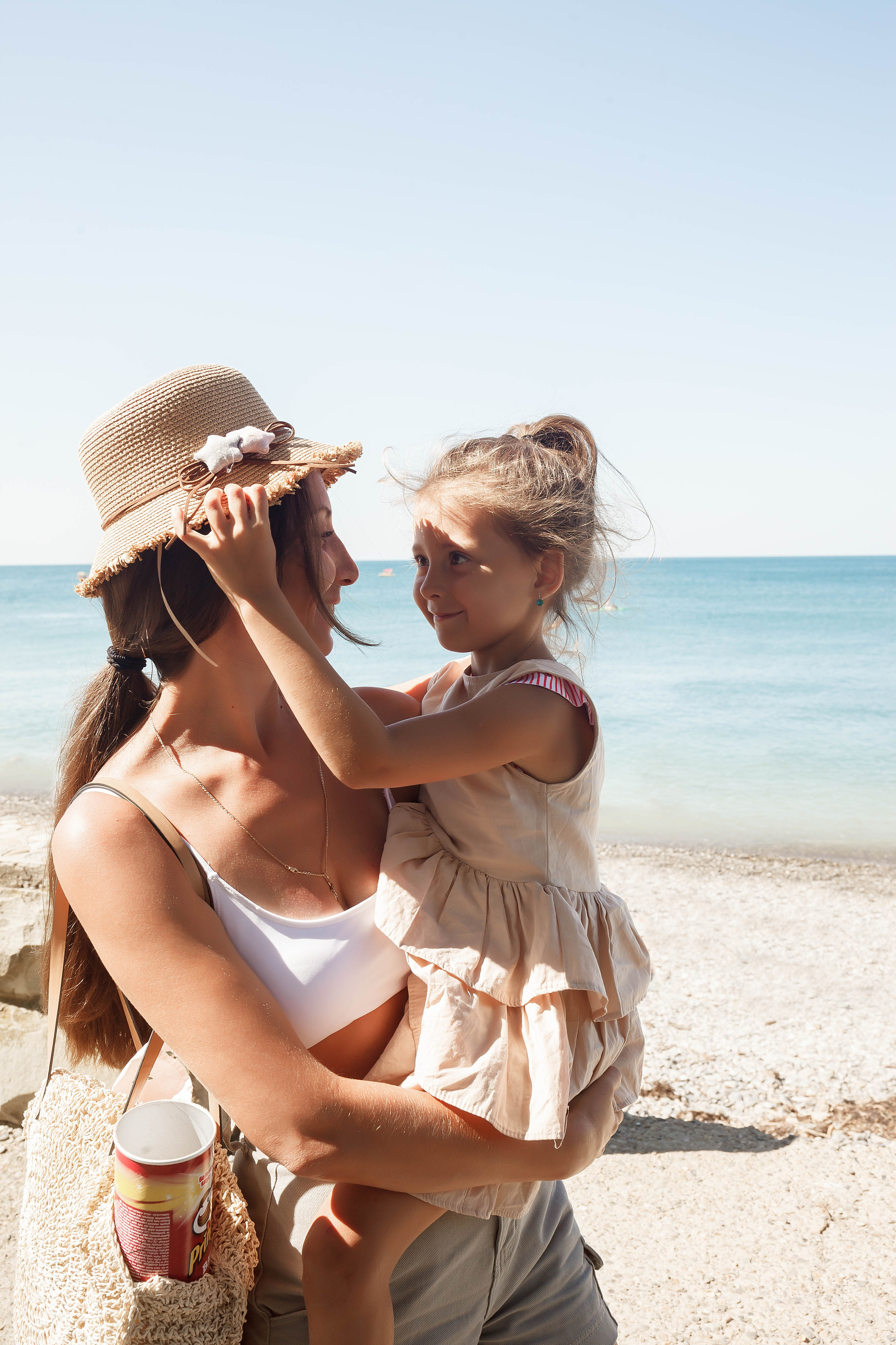 девочка поправляет шляпу маме и смотрит ей в глаза на задней фоне море