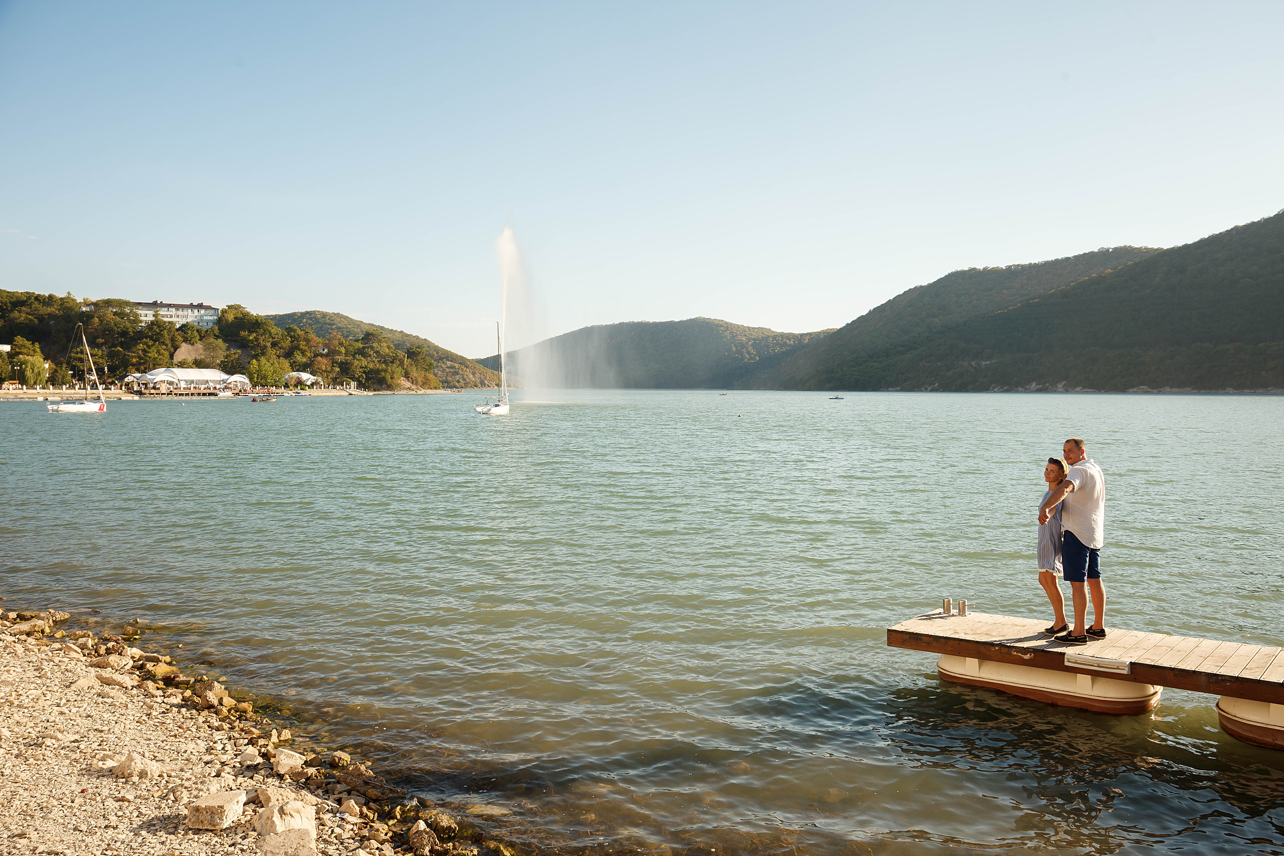 мужчина и женщина стоят обнявшись на пирсе на озере абрау