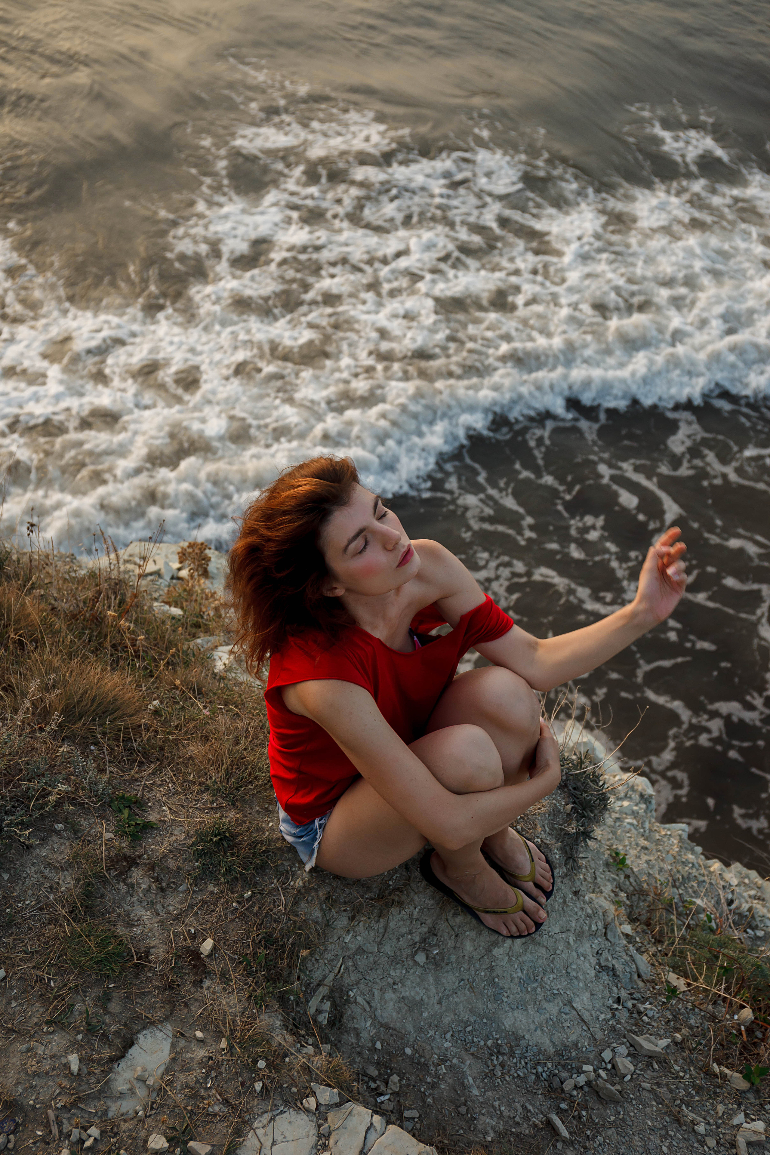 девушка в краснм сидит на скорне внизу волны она мечтает