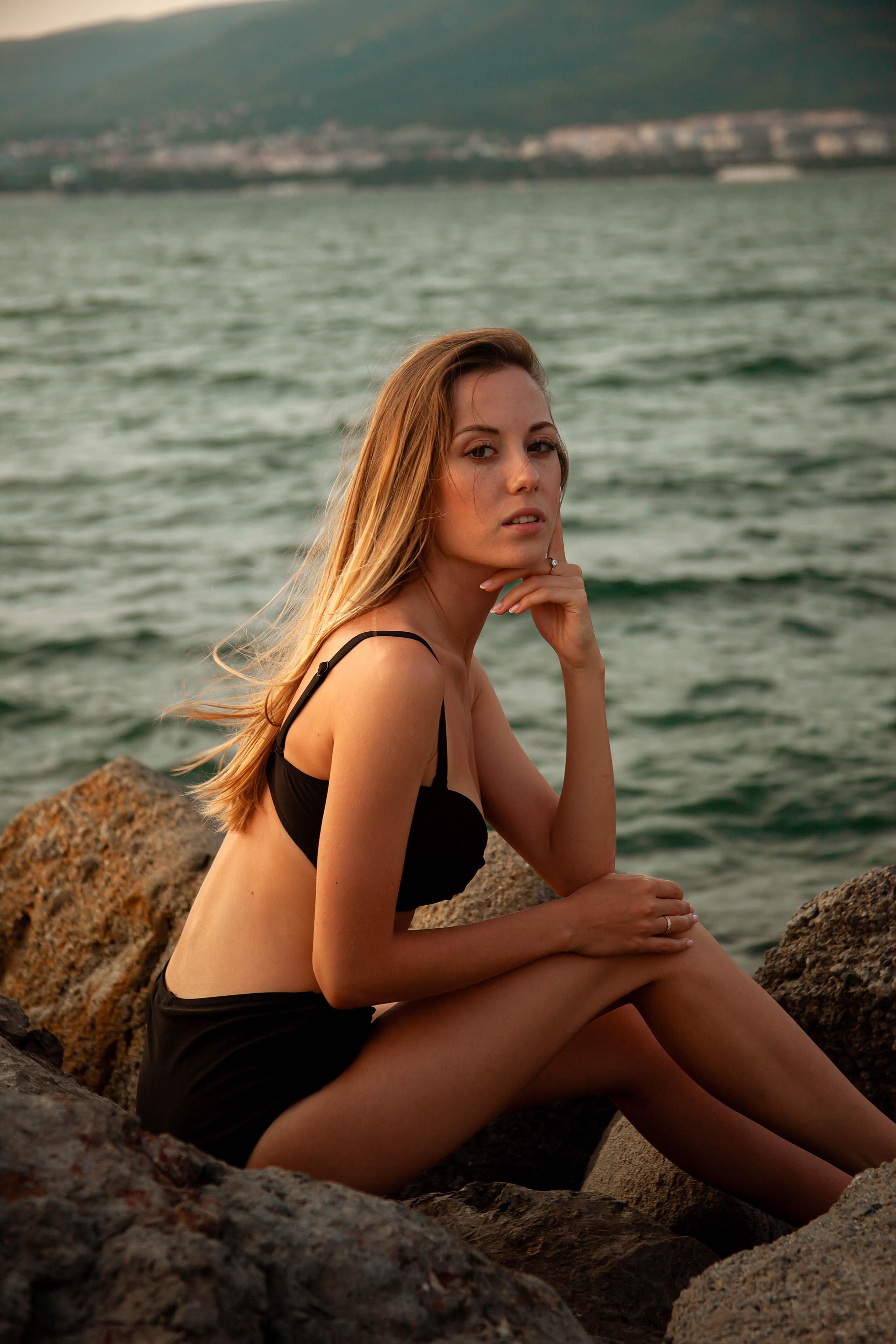 девушка с развивающимися волосами сидит на камне на пляже