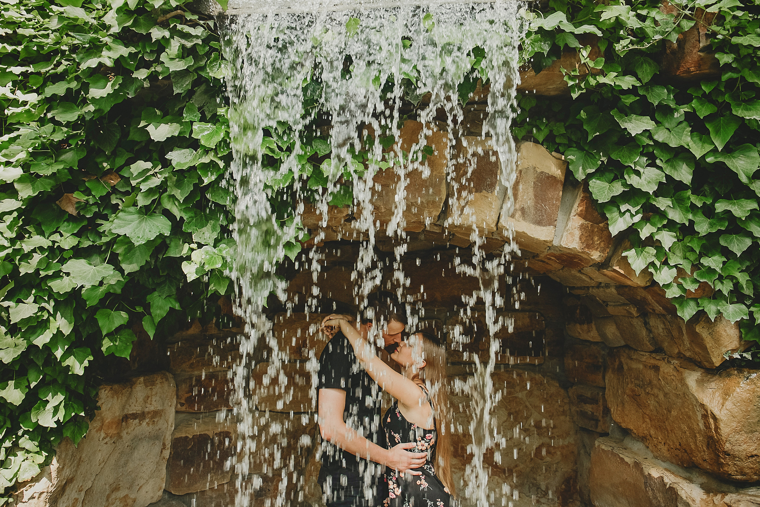 пара целуется под искусственным водопадом в старом парке