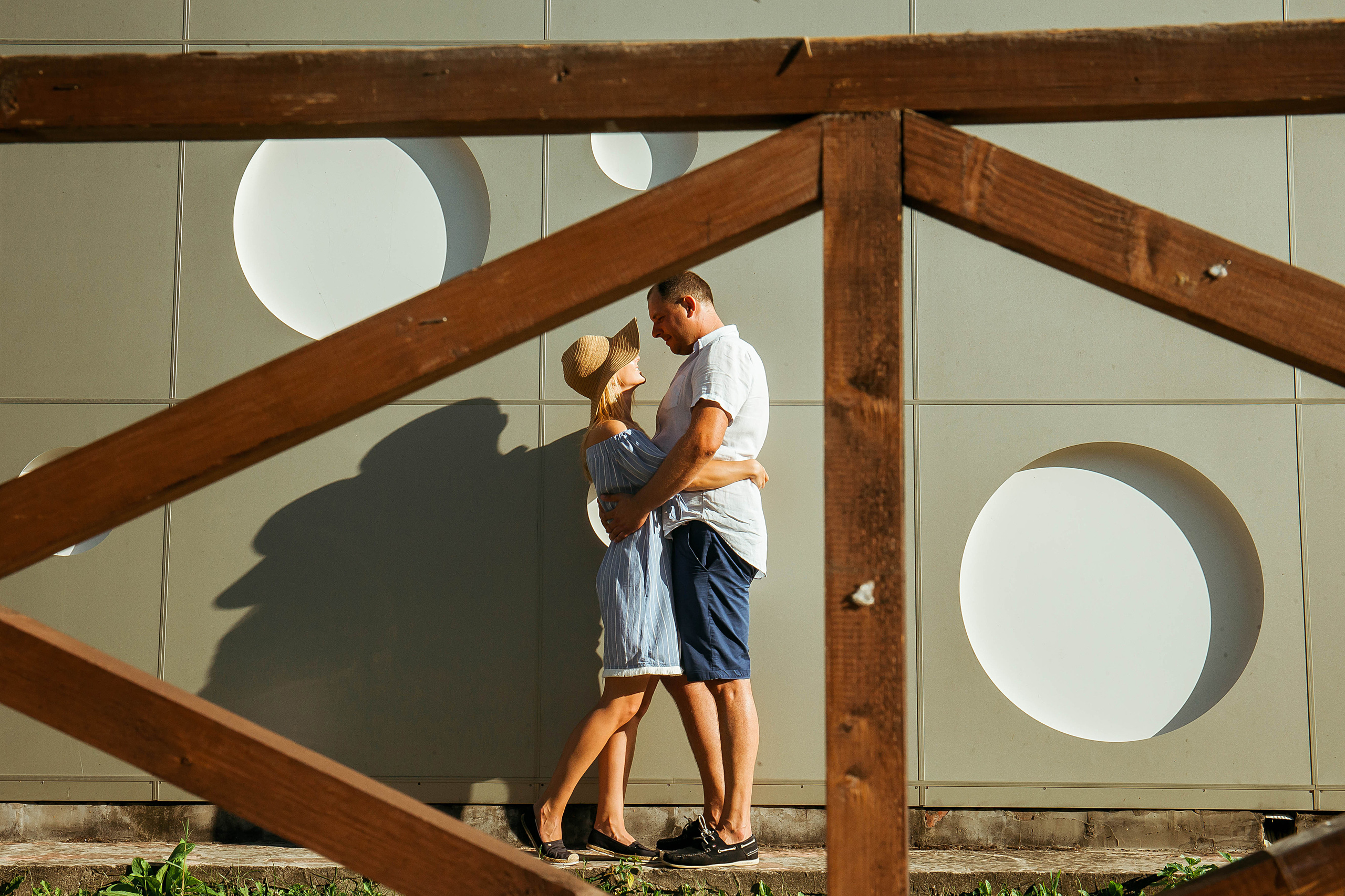 муж с женой стоят обнявшись у структурной стены в Абрау