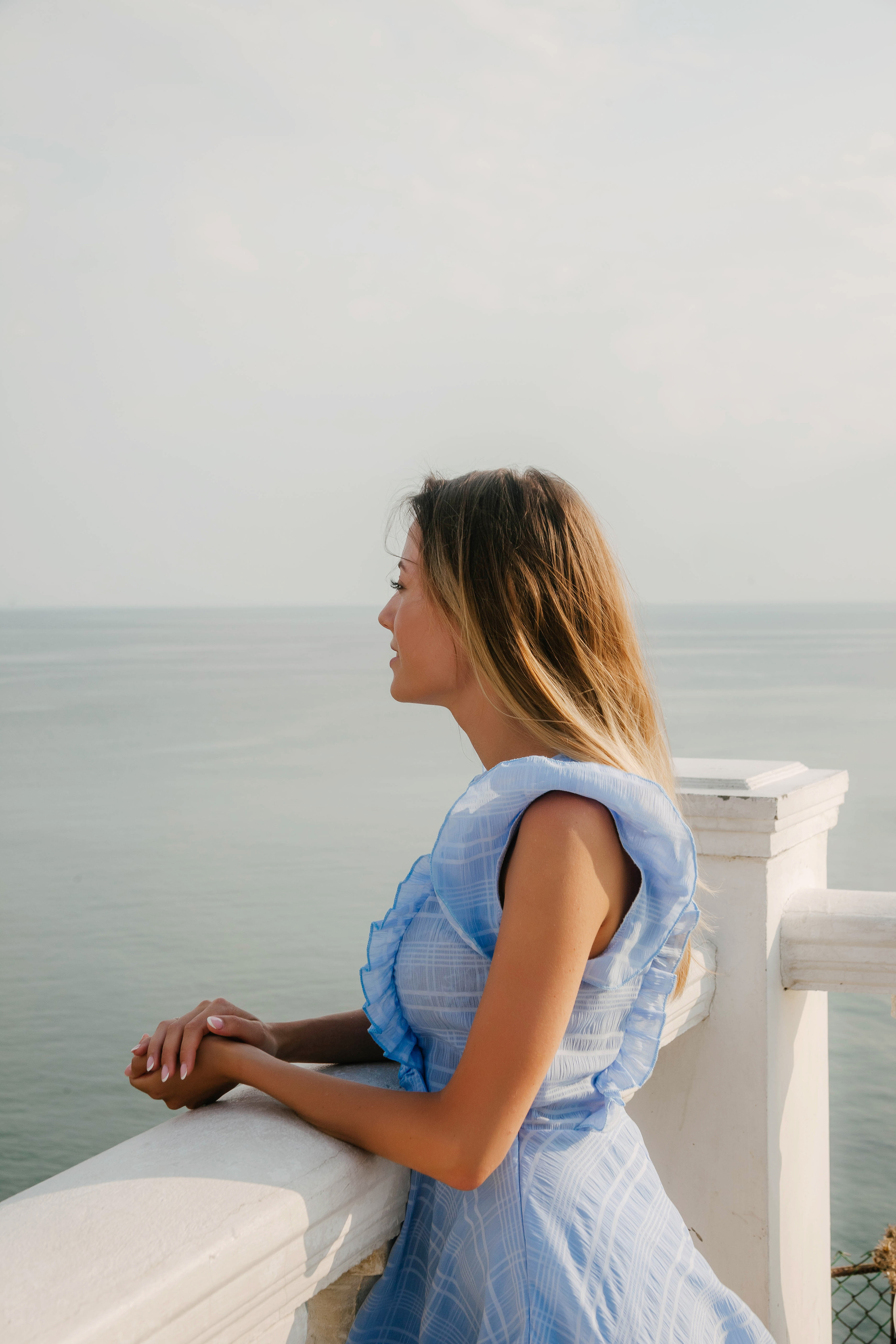 девушка в летнем голубом платье смотрит на море