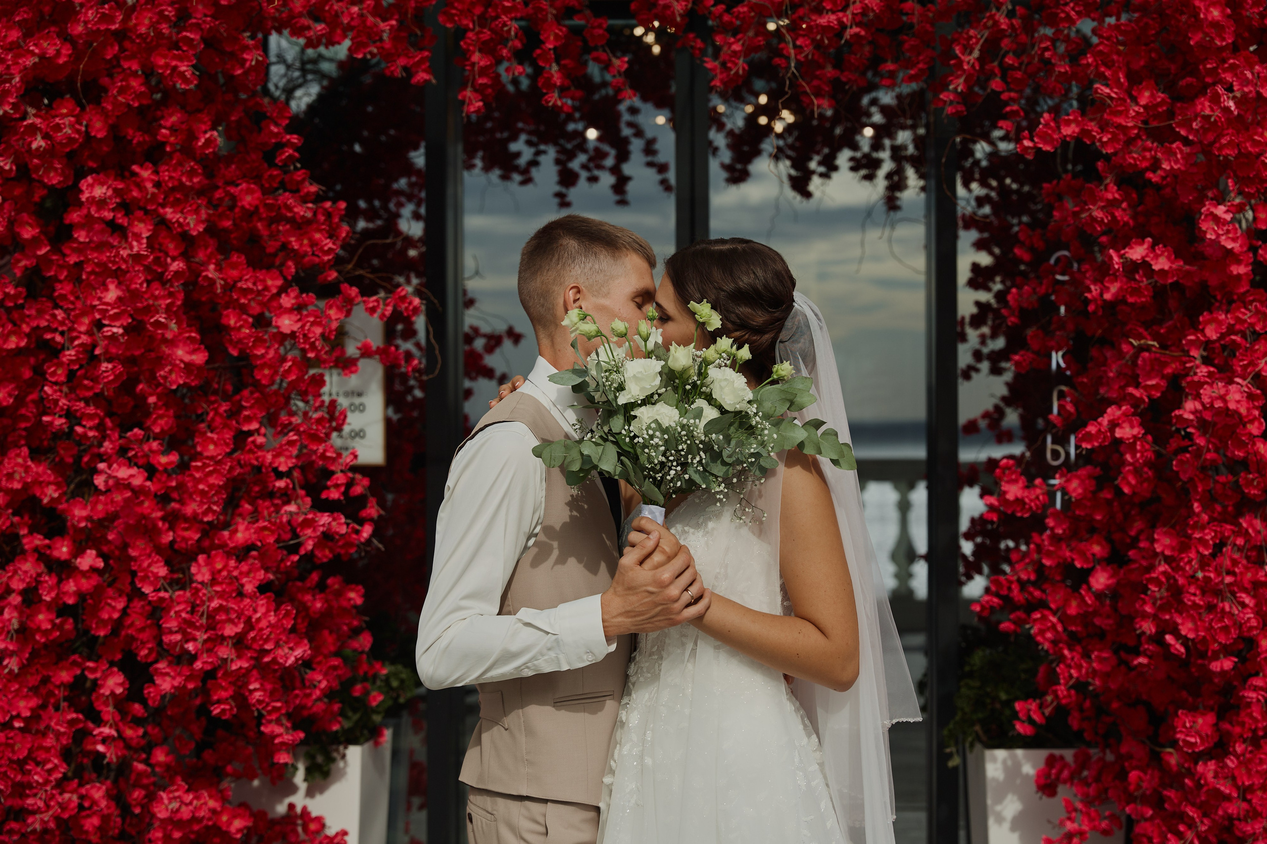 Жених и невеста прячут поцелуй за свадебным букетом