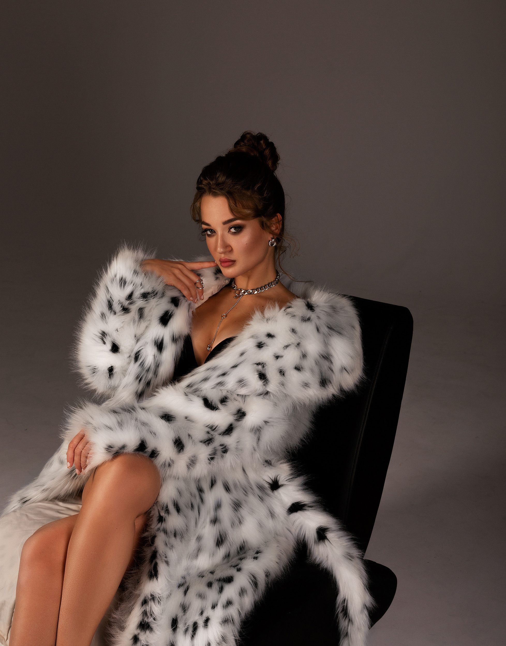 портрет девушки в студии в белой шубе в кресле на сером фоне