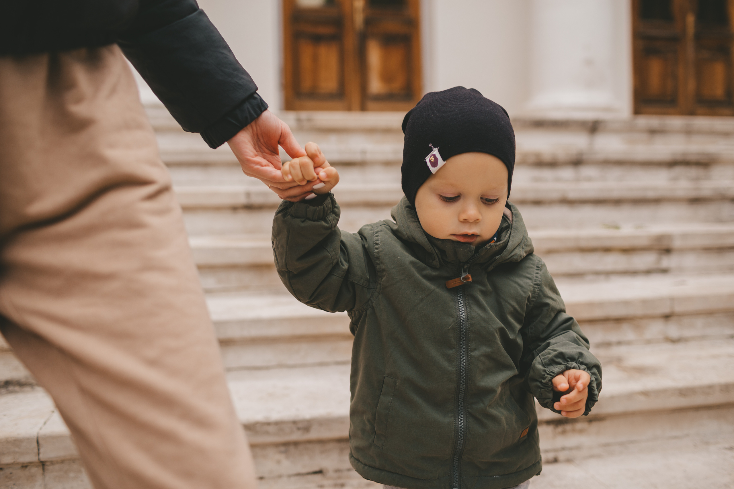 Мама с сыном идут за руку. Мальчик в зеленой футболке и синей шапке