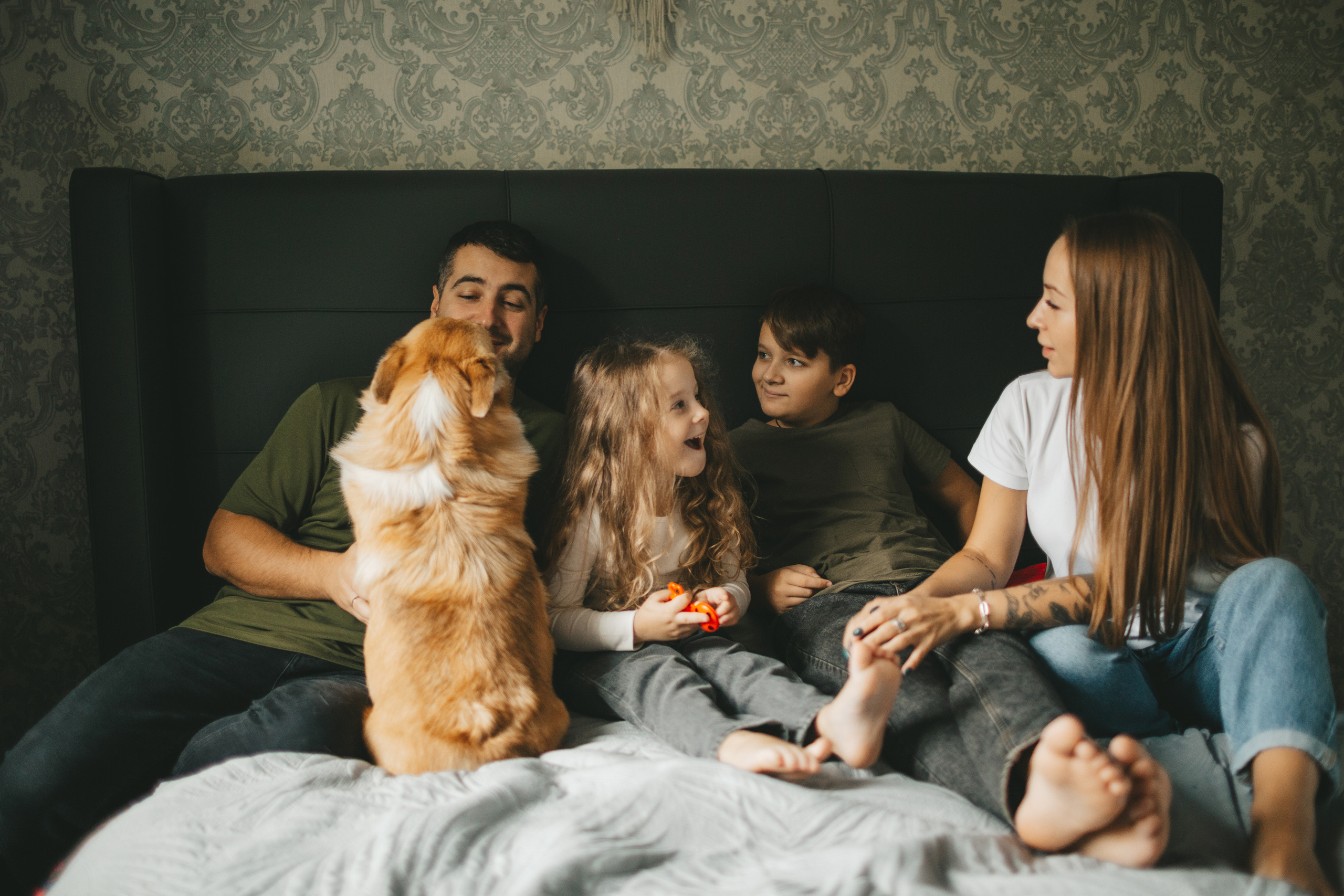 Семья сидит на кровати с собакой корги