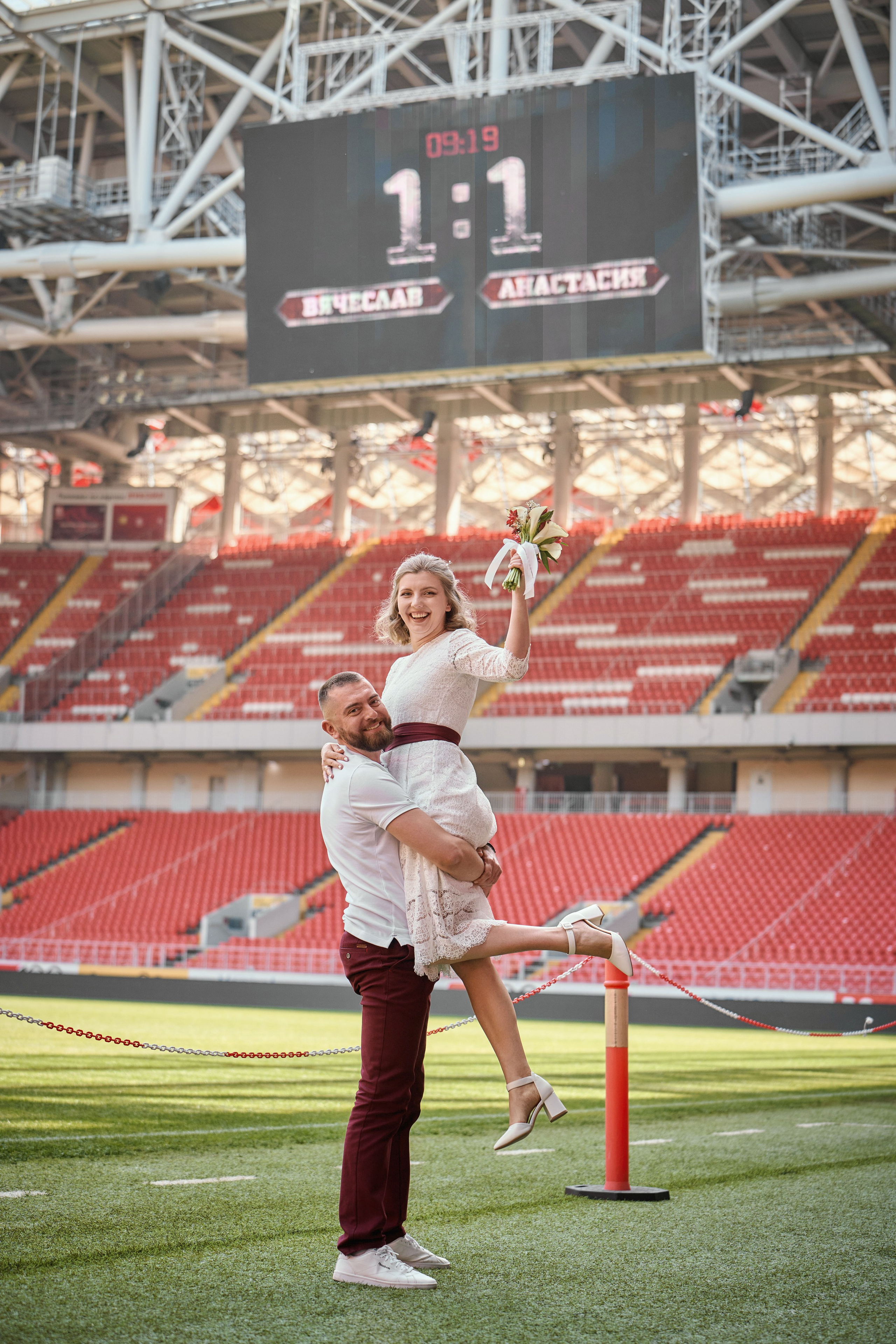 жених держит невесту на руках на стадионе Спартака, счёт на табло 1:1