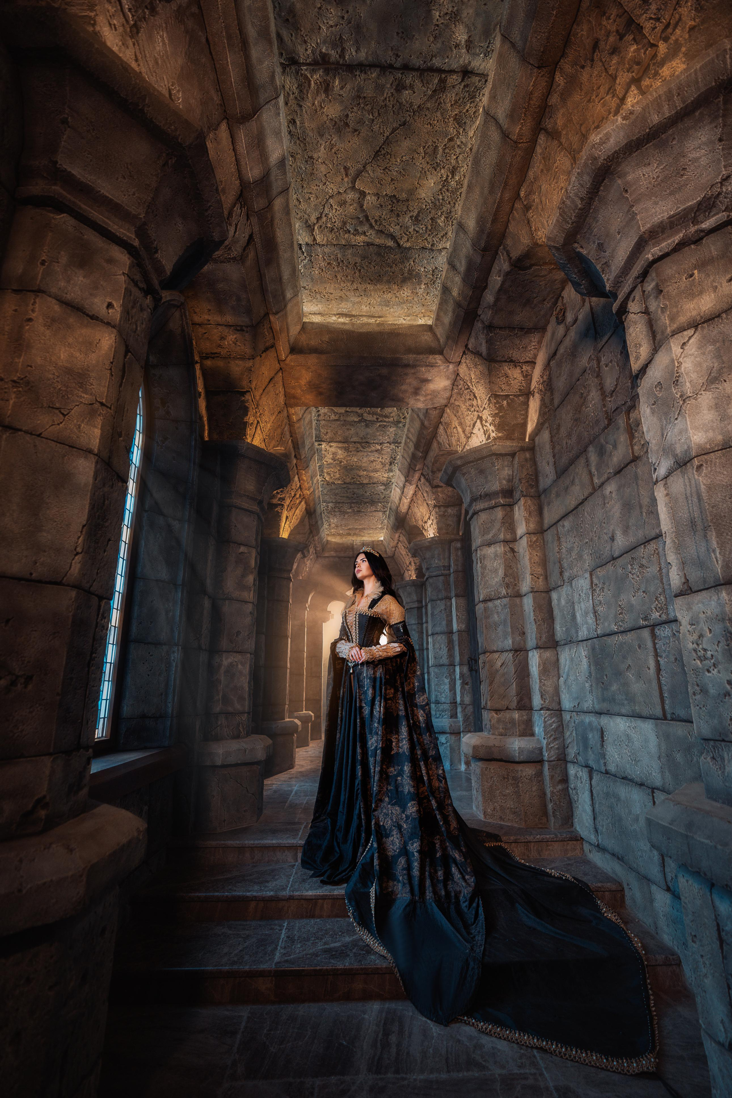девушка  в тёмном платье поднимается по каменной лестнице внутри замка Гарибальди, придавая кадру оттенок средневековой тайны.