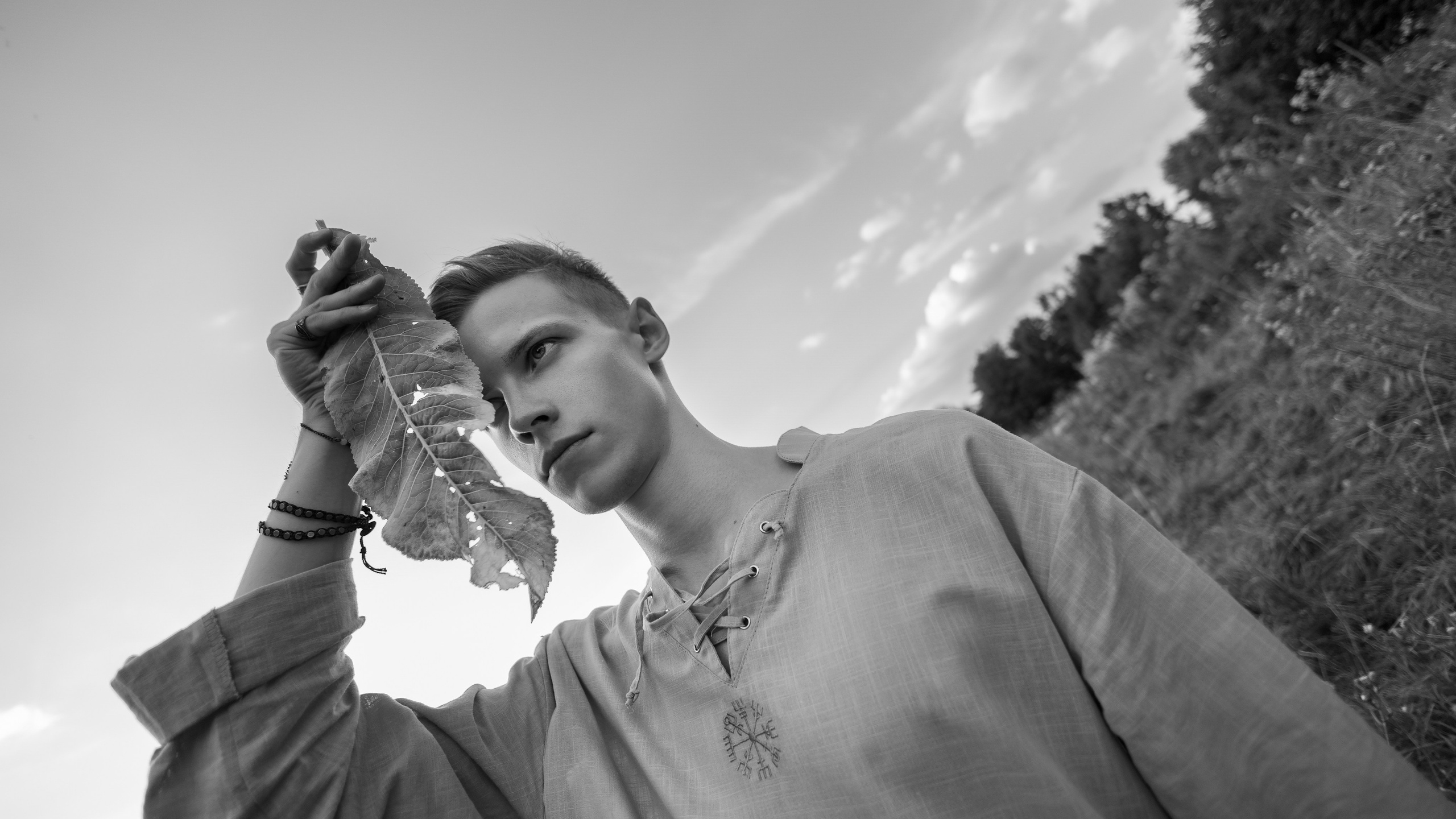 Молодой парень держит лист хрена у лица и смотрит вдаль