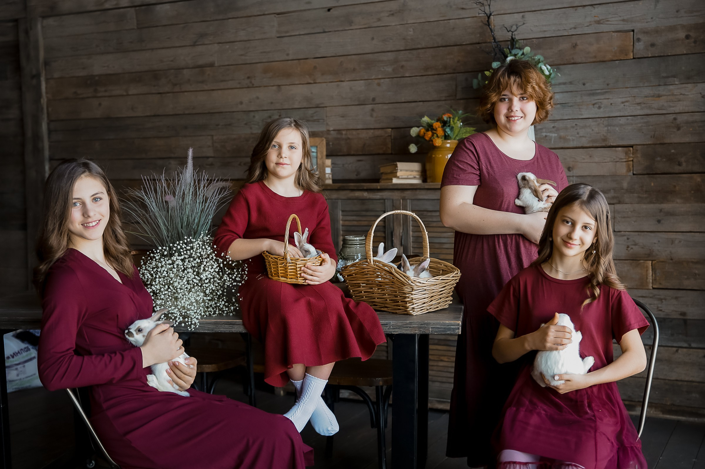Несколько девочек в бордовых платьях в студии, в стиле Шале держат в руках белых кроликов.