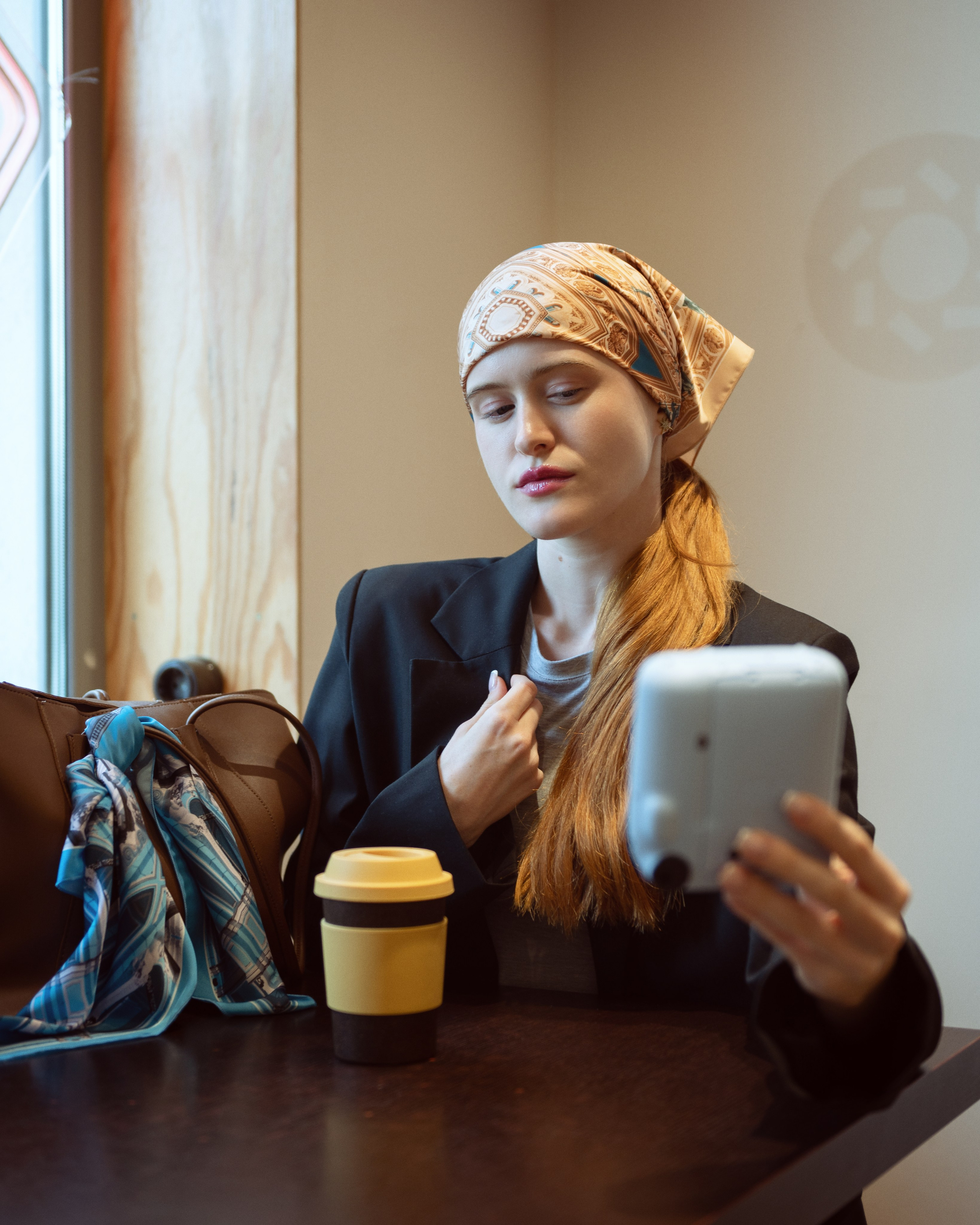 Красивая девушка в ярко-желтом платке сидит в кофейне и  снимает себя на Instax