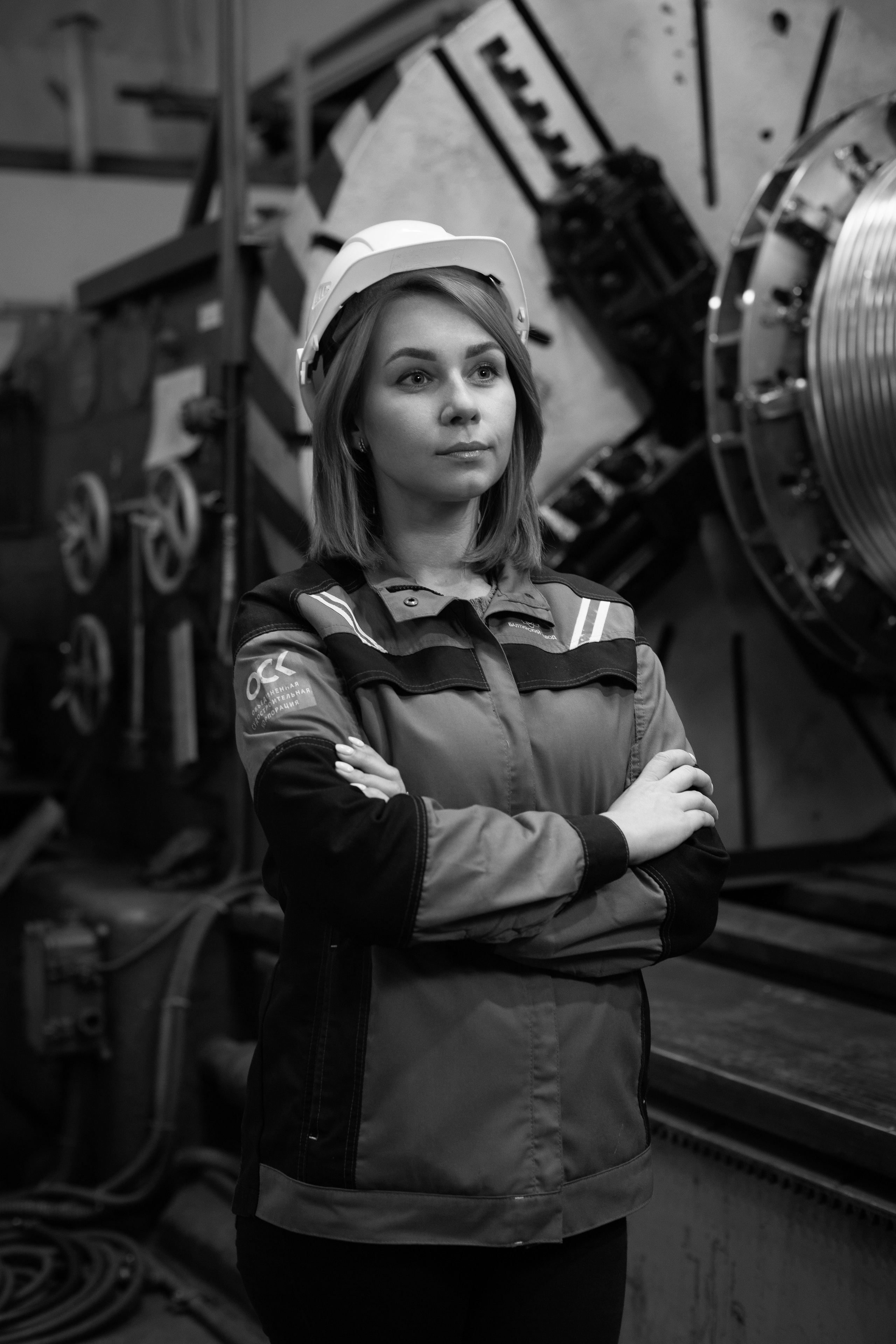 Молодая девушка в каске фотографируется на производстве.