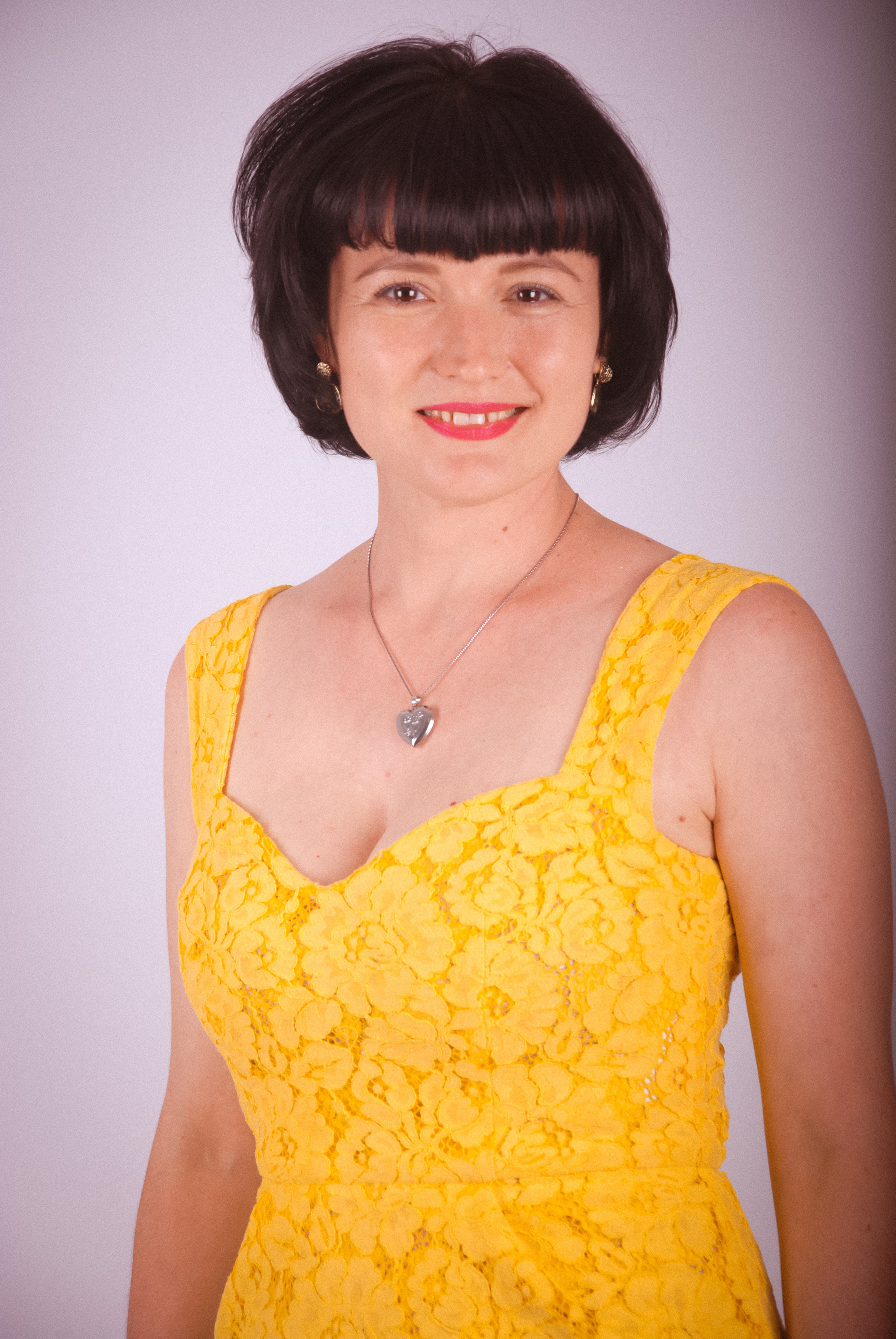 Улыбающаяся девушка в ярком желтом платье с малиновой помадой на губах  позирует  фотографу 