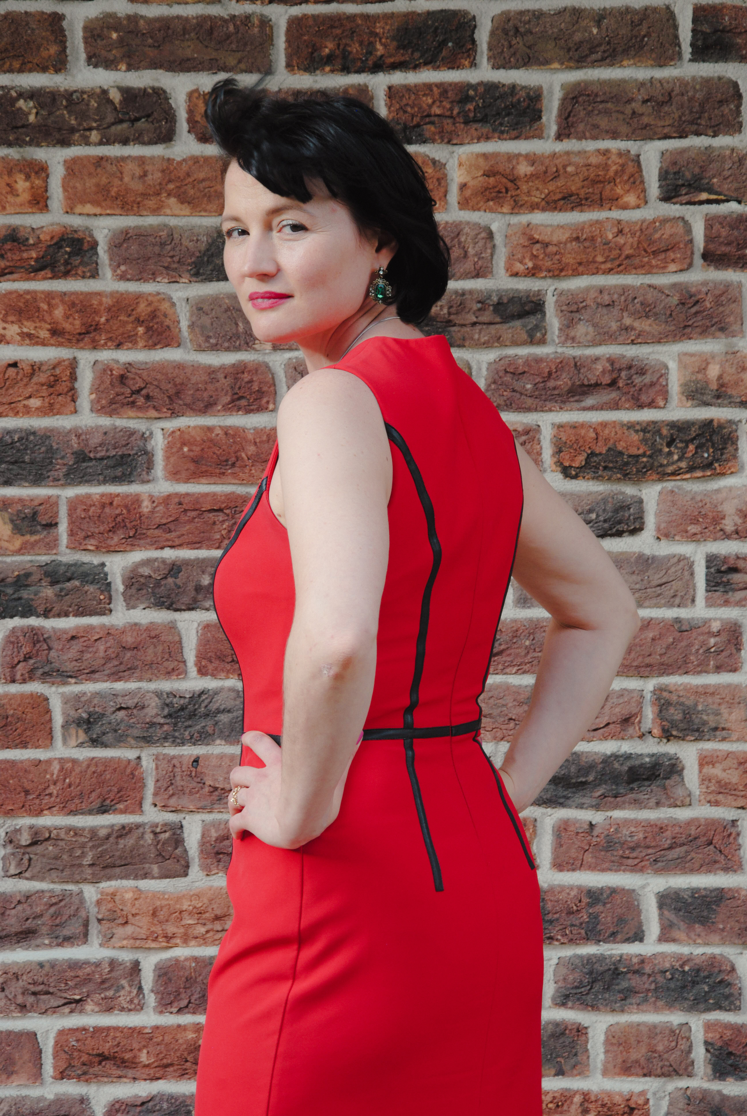 Модель в красном платье на фоне кирпичной стены в стиле лофт стоит развернувшись полубоком