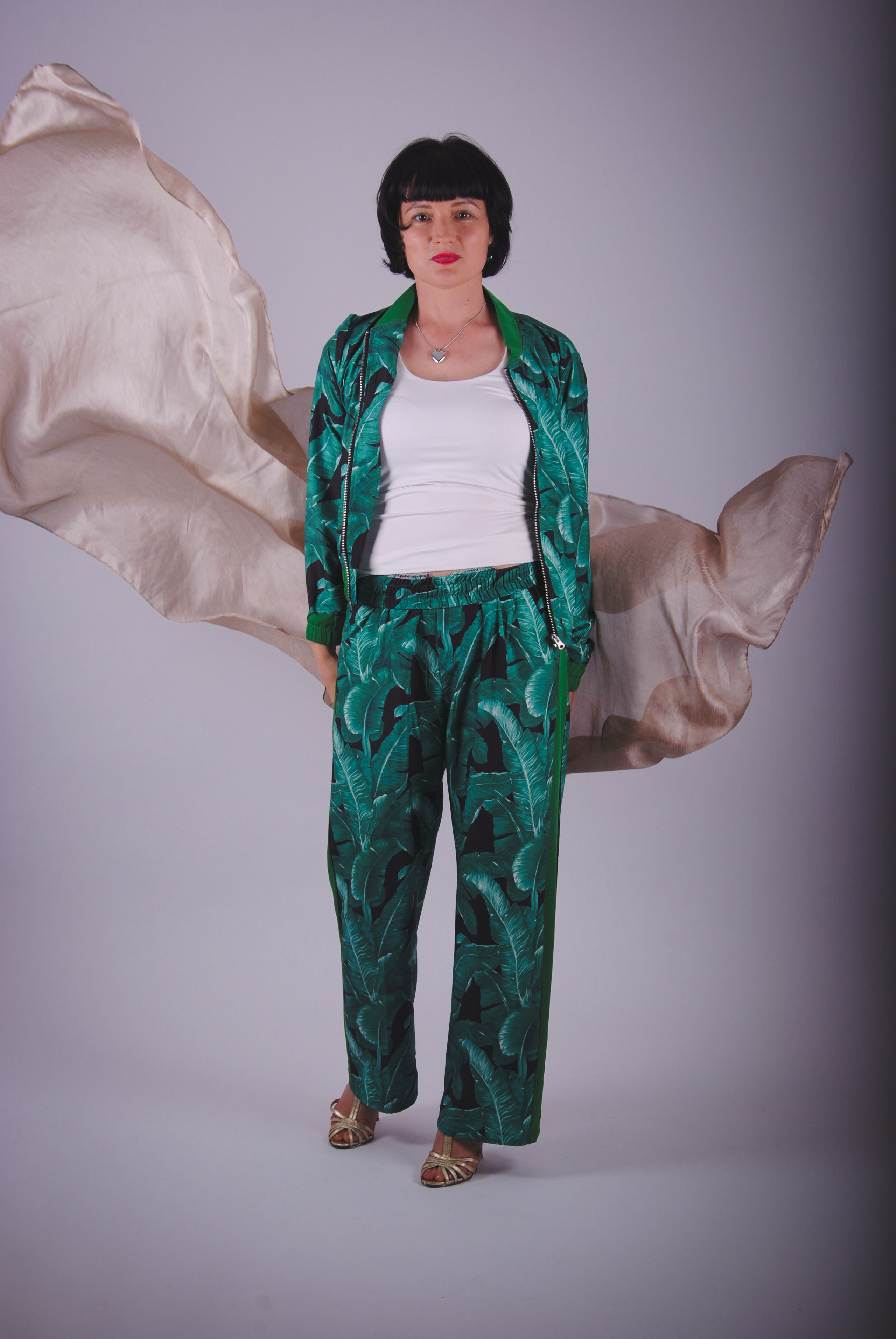 Девушка в изумрудно-зеленом брючном костюме с малиновой помадой на губах с развивающимся бежевым шелковым платком