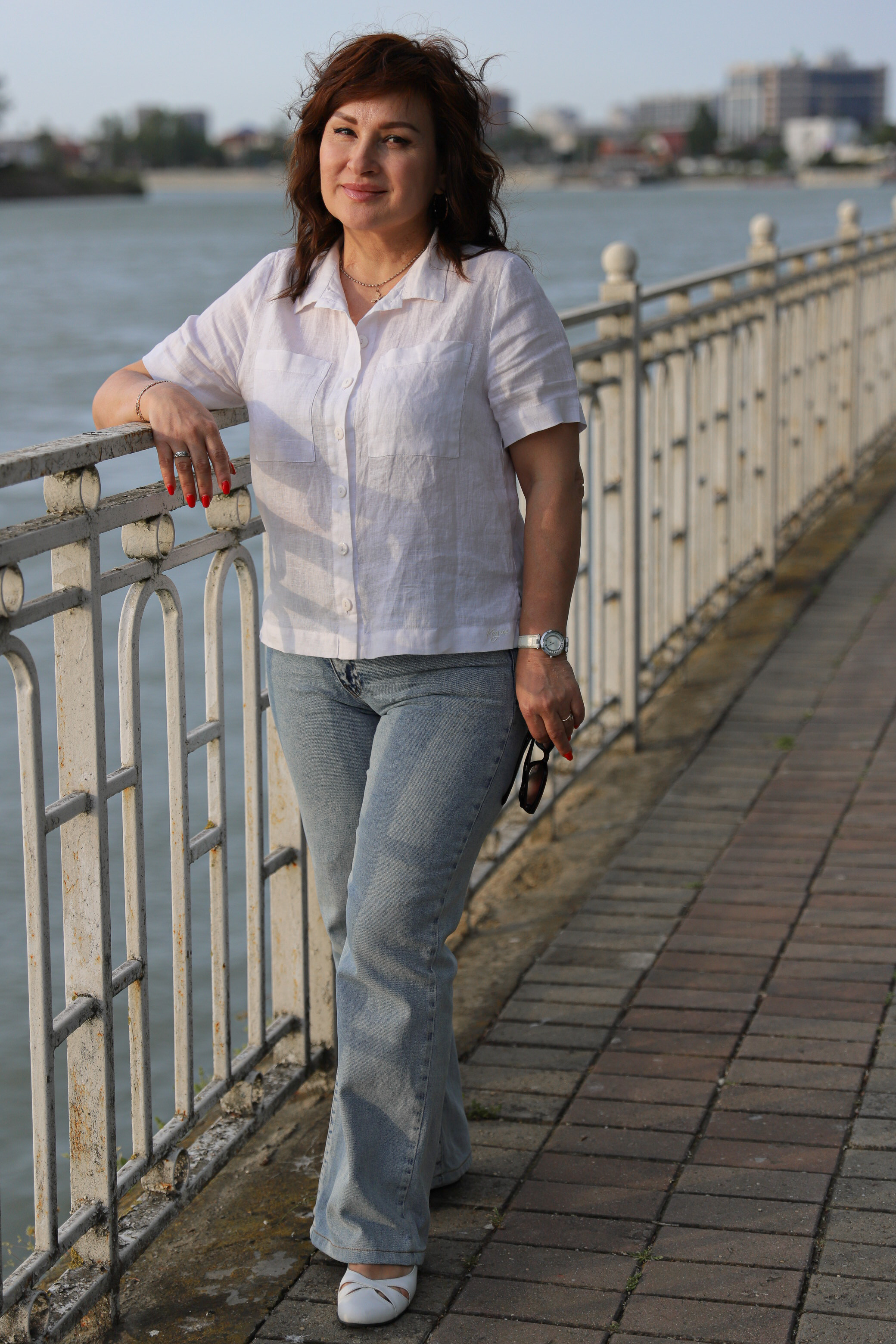 Улыбчивая женщина  на фоне реки Кубань на набережной у красивого резного забора