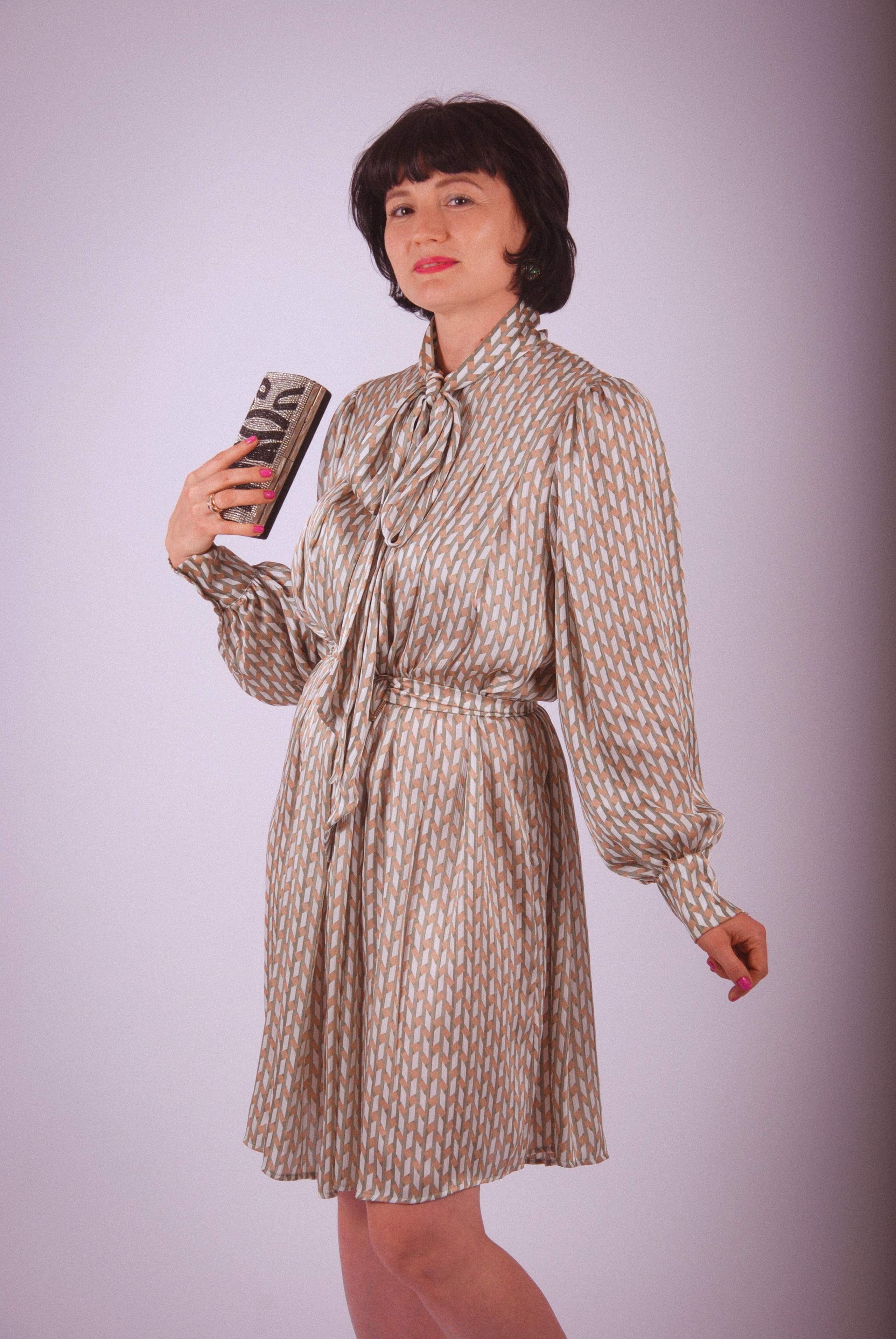 Девушка с маленькой сумочкой в платье с бантом приветливо улыбается 