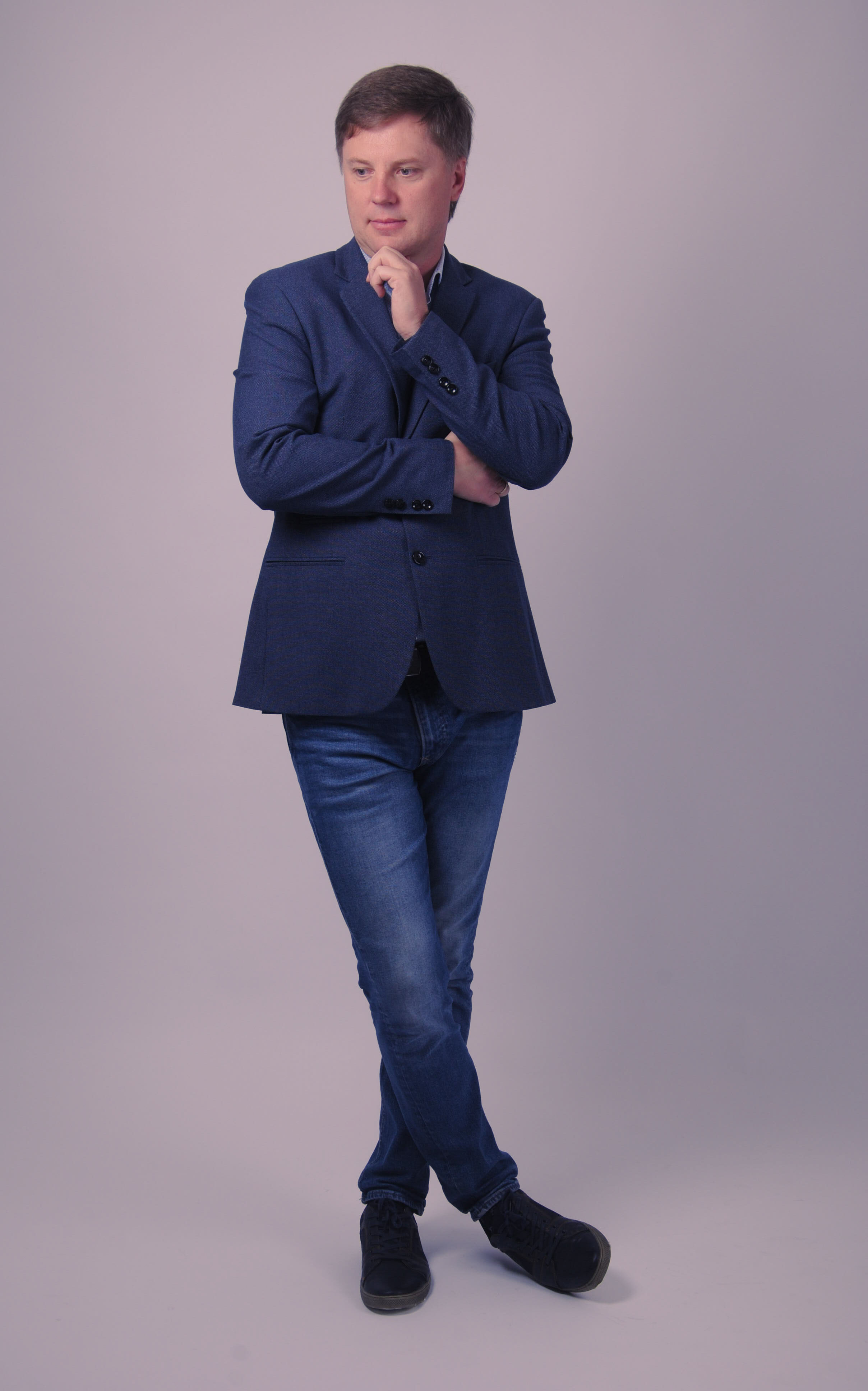 Молодой человек одет  в стиле лофт и стоит в закрытой позе, т.е. скрестил руки и ноги