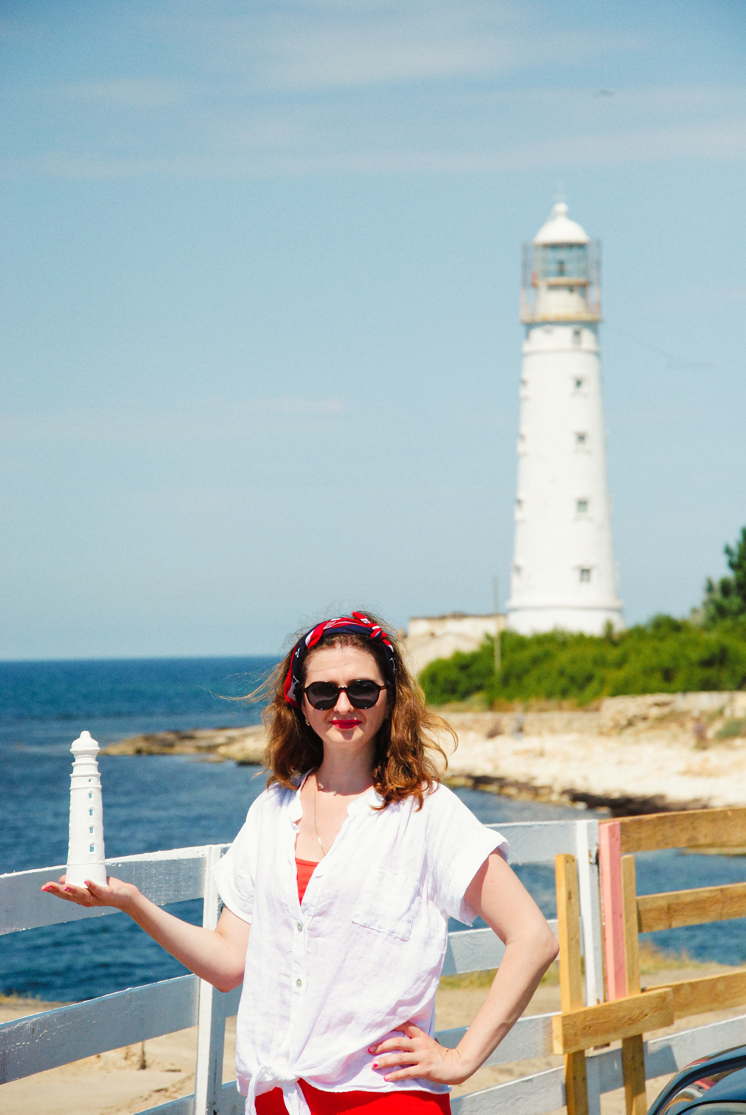 Девушка в черных очках в морском стиле держит гипсовую уменьшенную копию маяка на  крайней западной точки Крыма