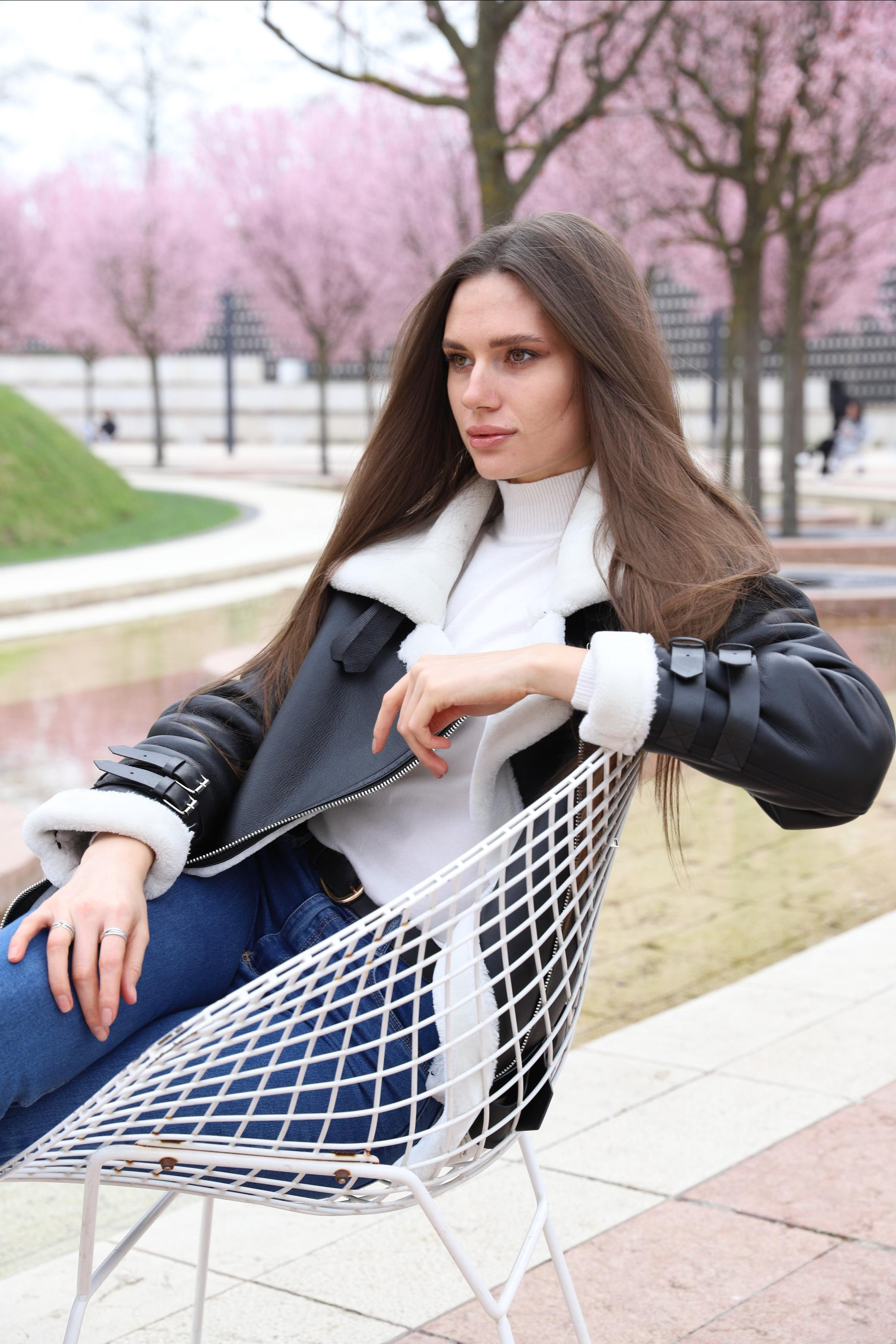 Модель с длинными русыми волосами сидит в весеннем парке на кресле