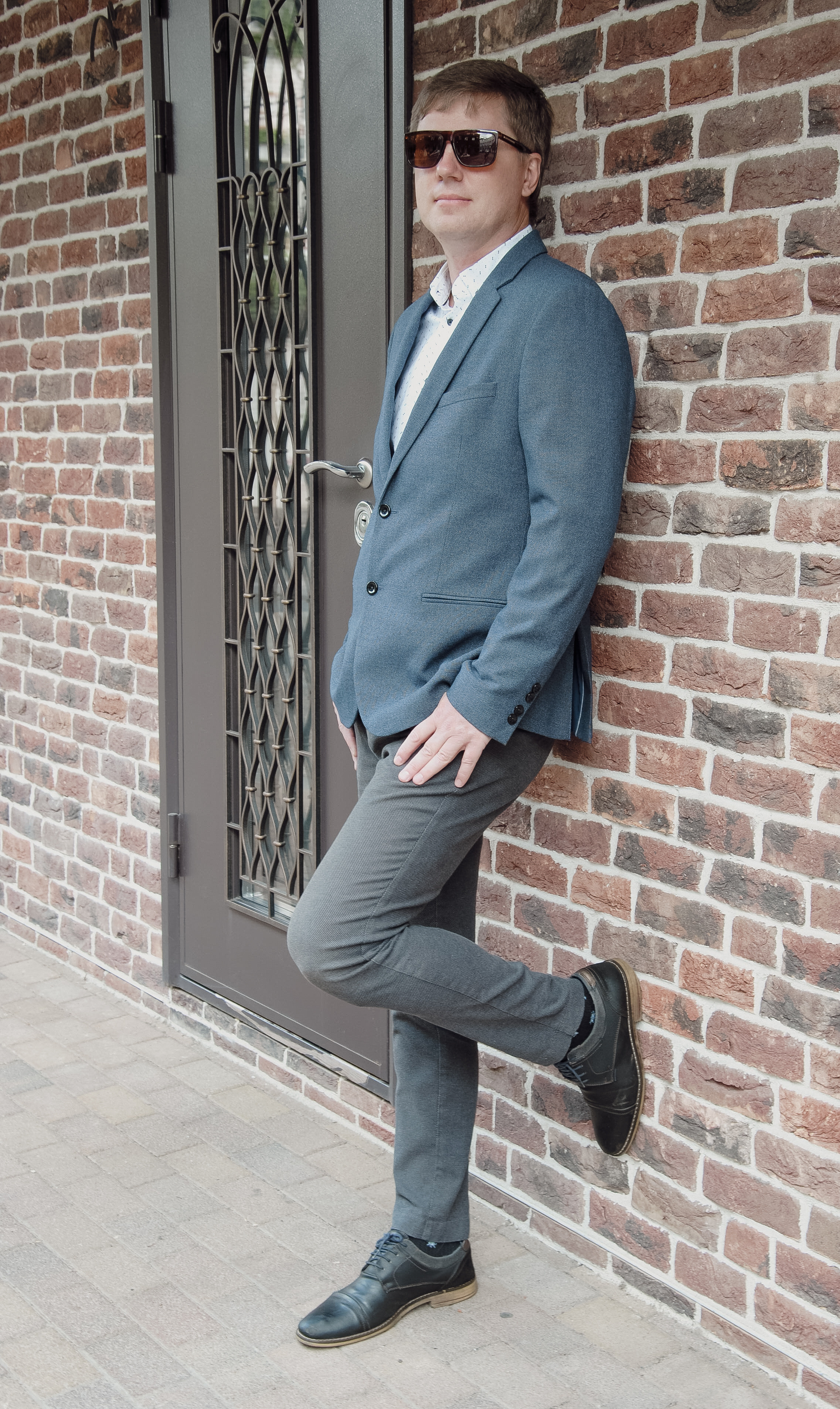 Стильный  мужчина стоит у кирпичной стены на заднем плане железная кованая дверь