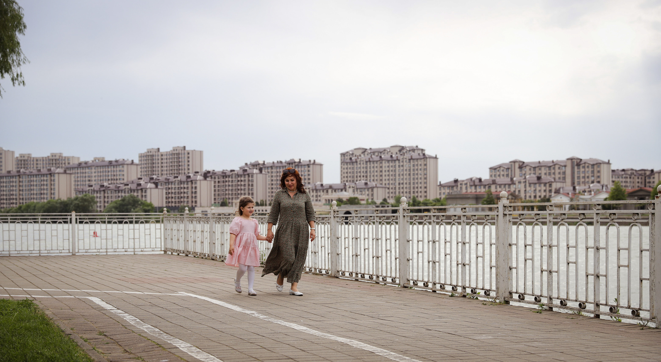 Бабушка и внучка гуляют по набережной кубанской реки, обмениваясь улыбками и хорошим настроением.
