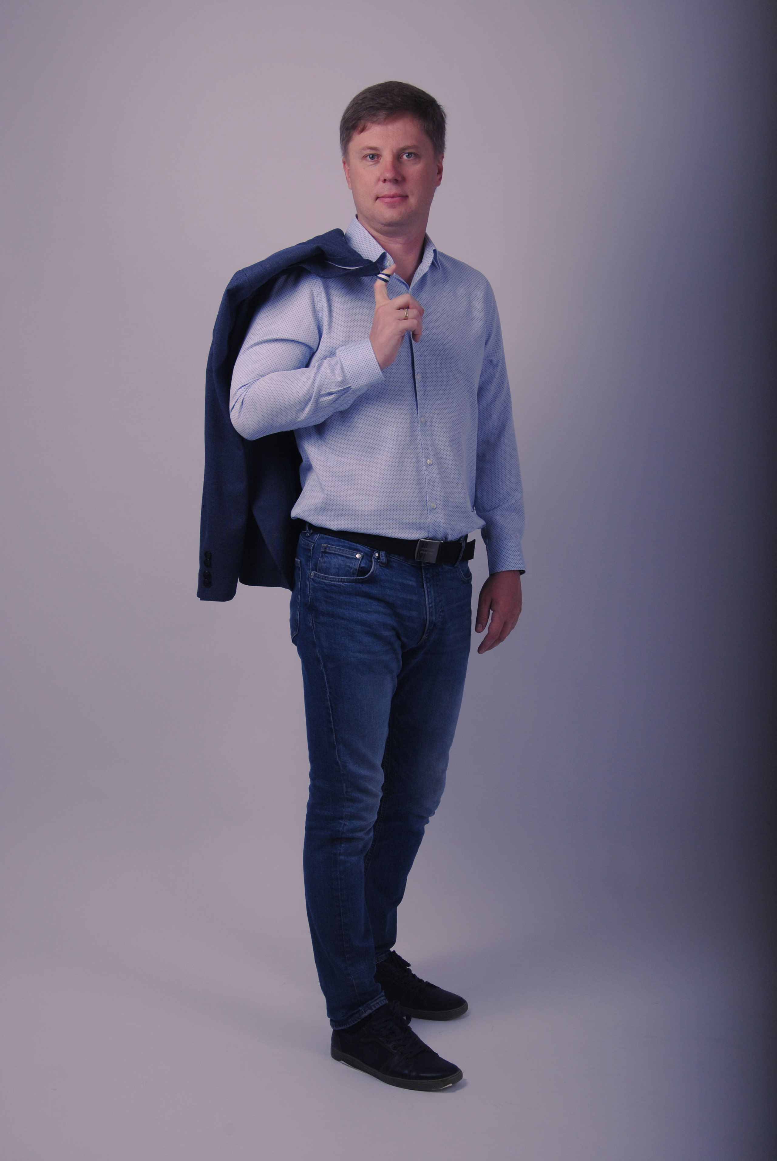 Модель позирует в джинсах и светлой рубашке, закинув за плечо пиджак