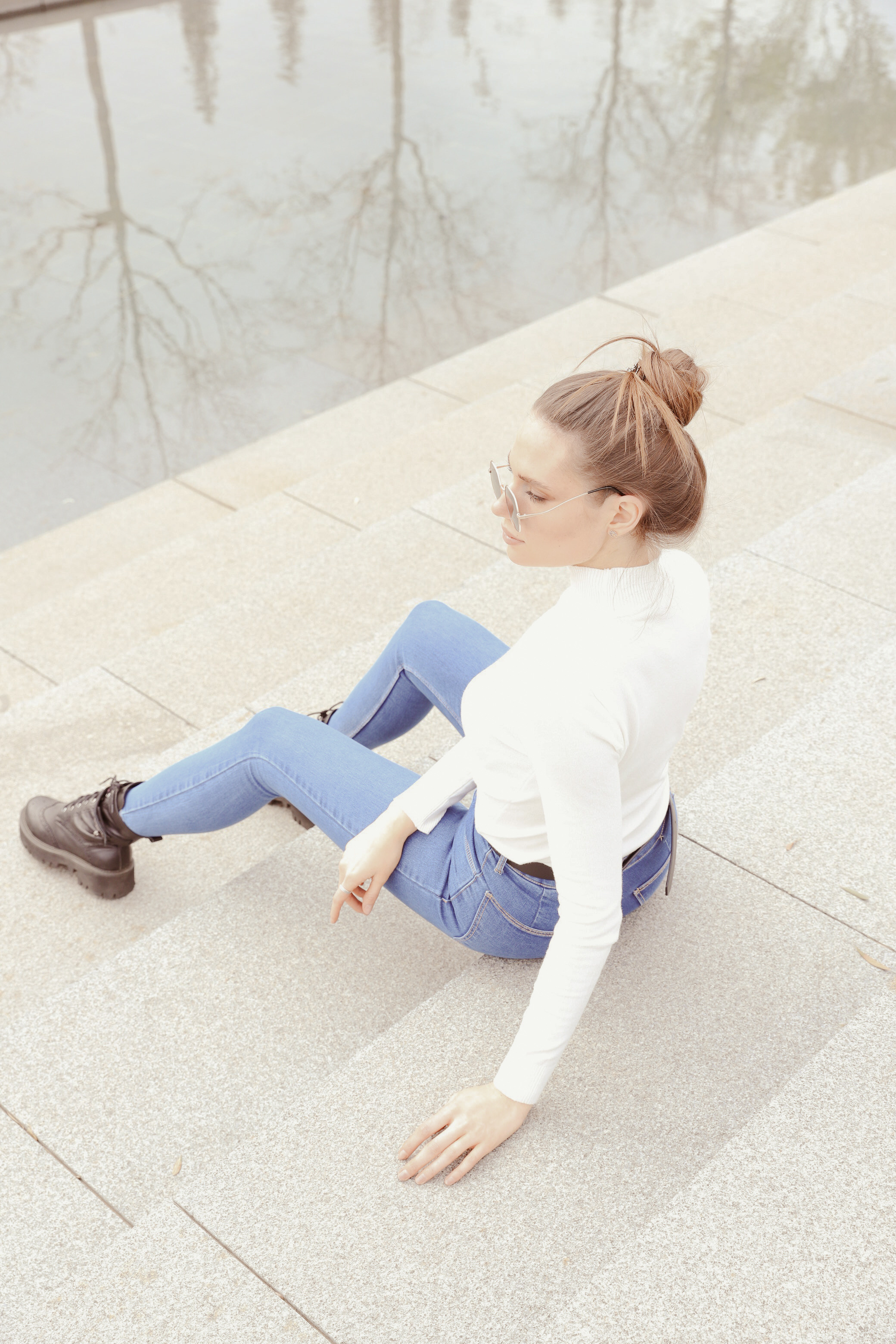 Утонченная девушка сидит на белых ступенях около воды