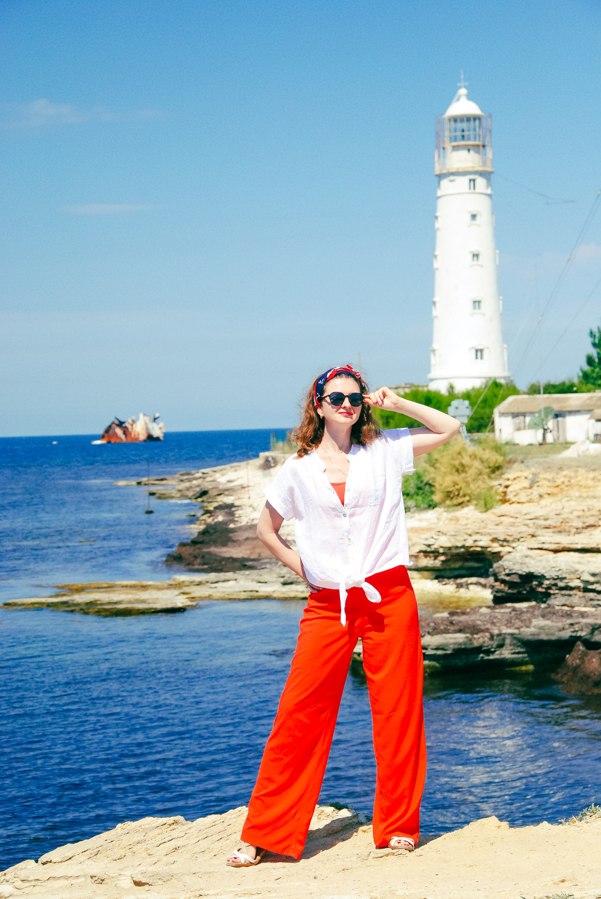 Девушка в красных штанах позирует на фоне белого маяка вблизи села Оленевка Крым