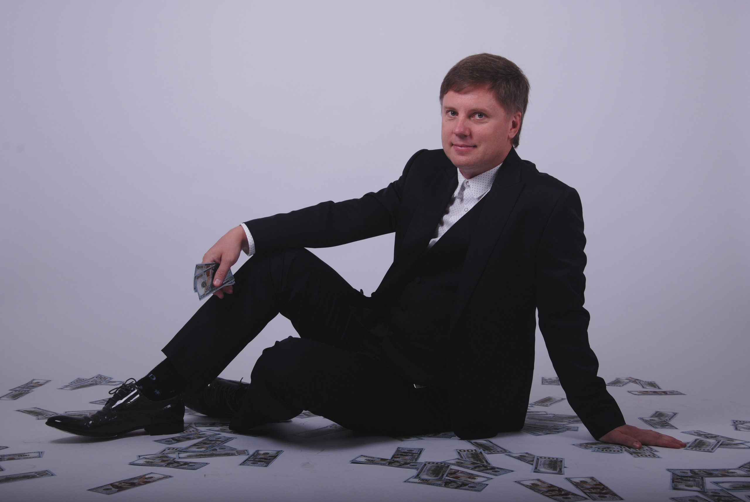 Бизнесмен в строгом костюме сидит на деньгах
