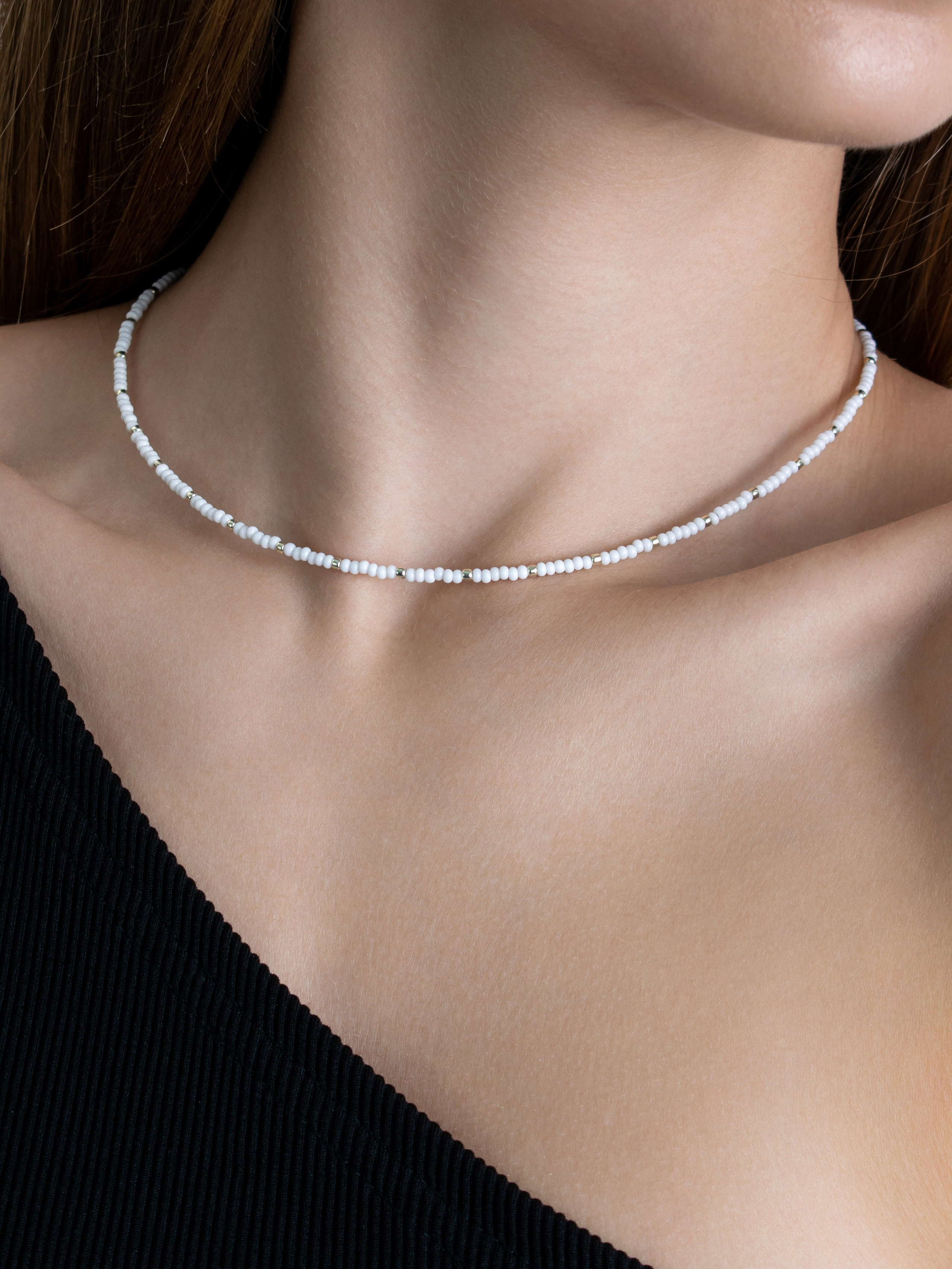 Чокер из белого бисера на шее девушки в черном платье