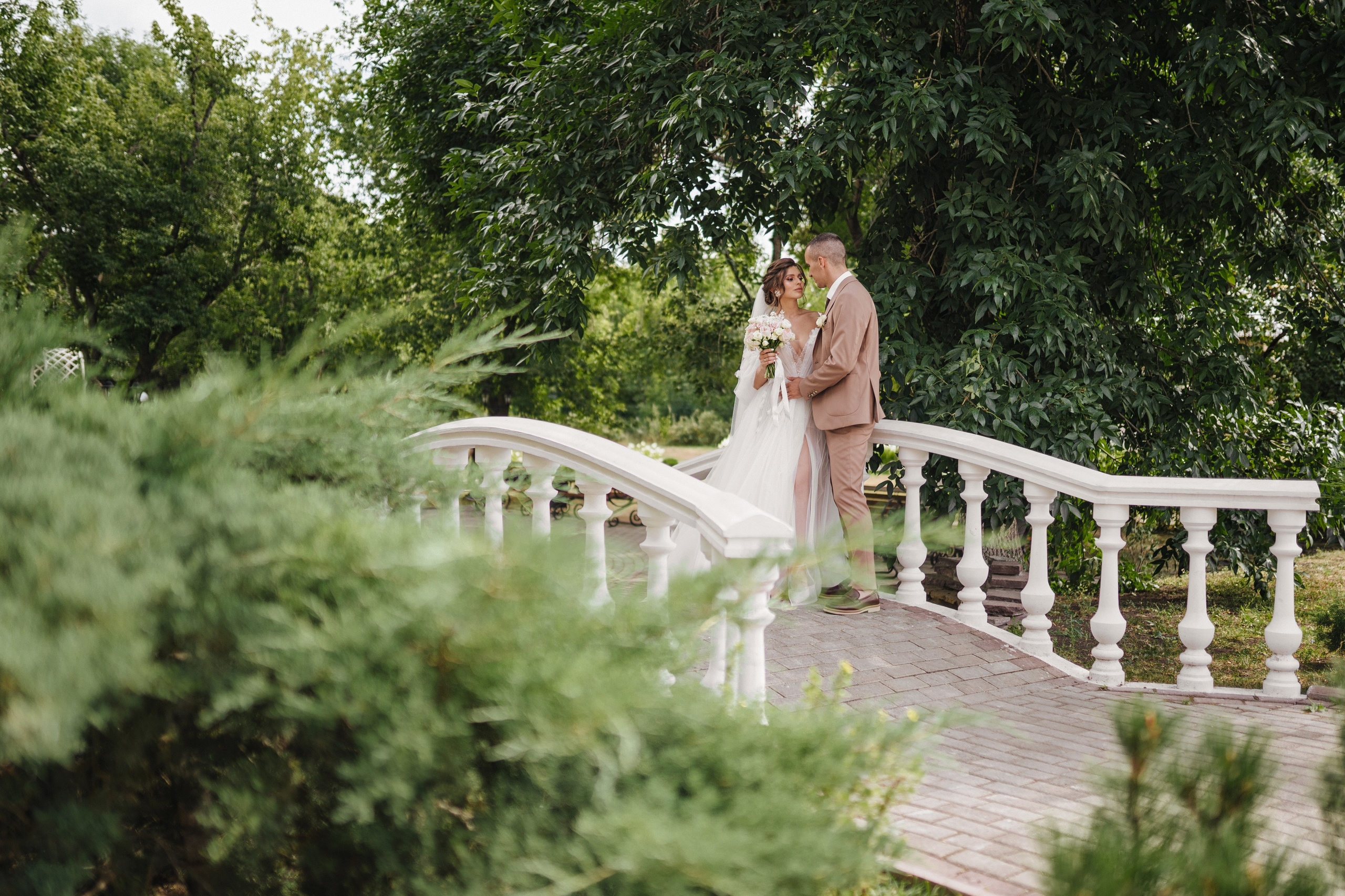 Жених и невеста обнимаются на мосту в парке