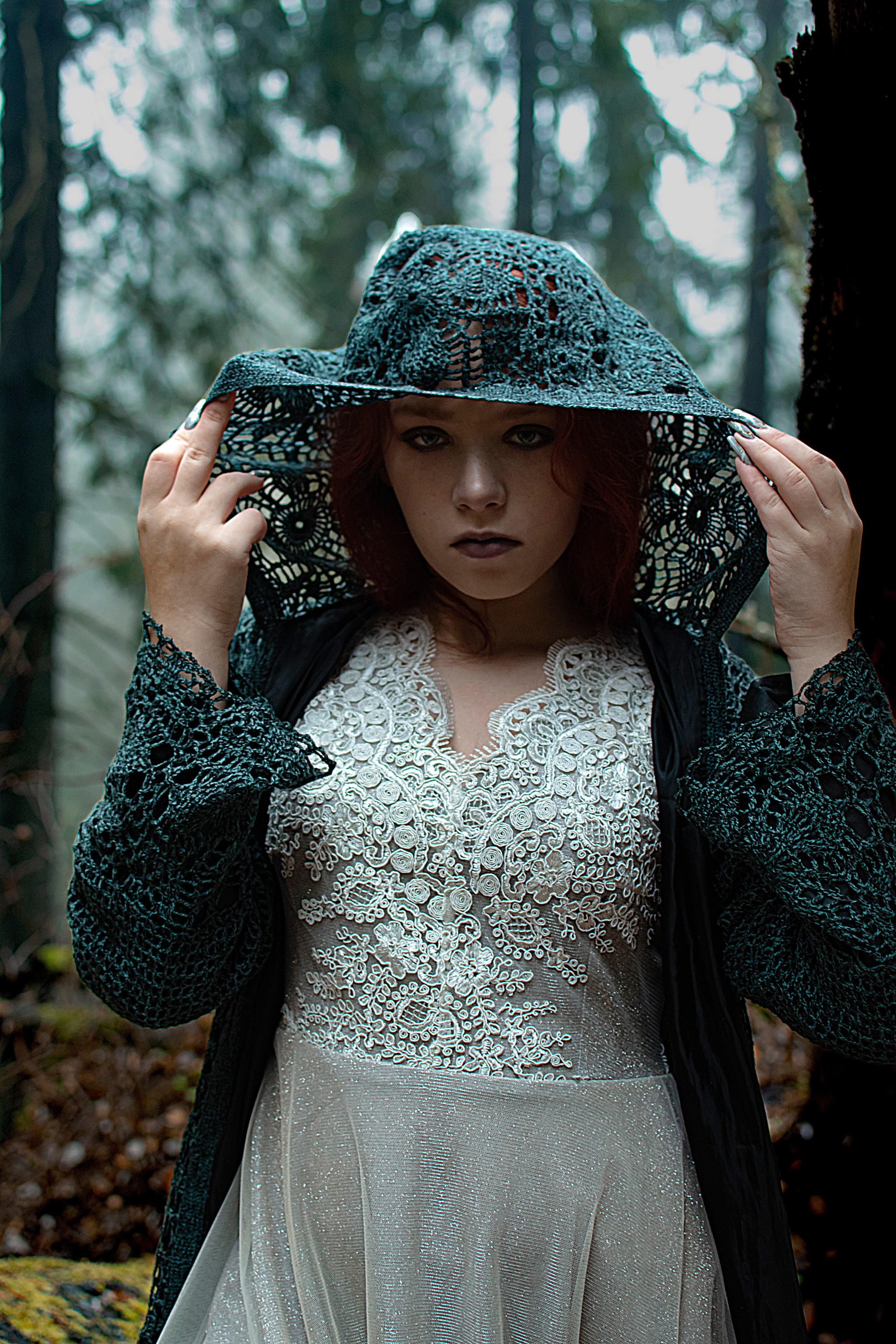 Девушка смотрит сквозь капюшон плаща в лесу