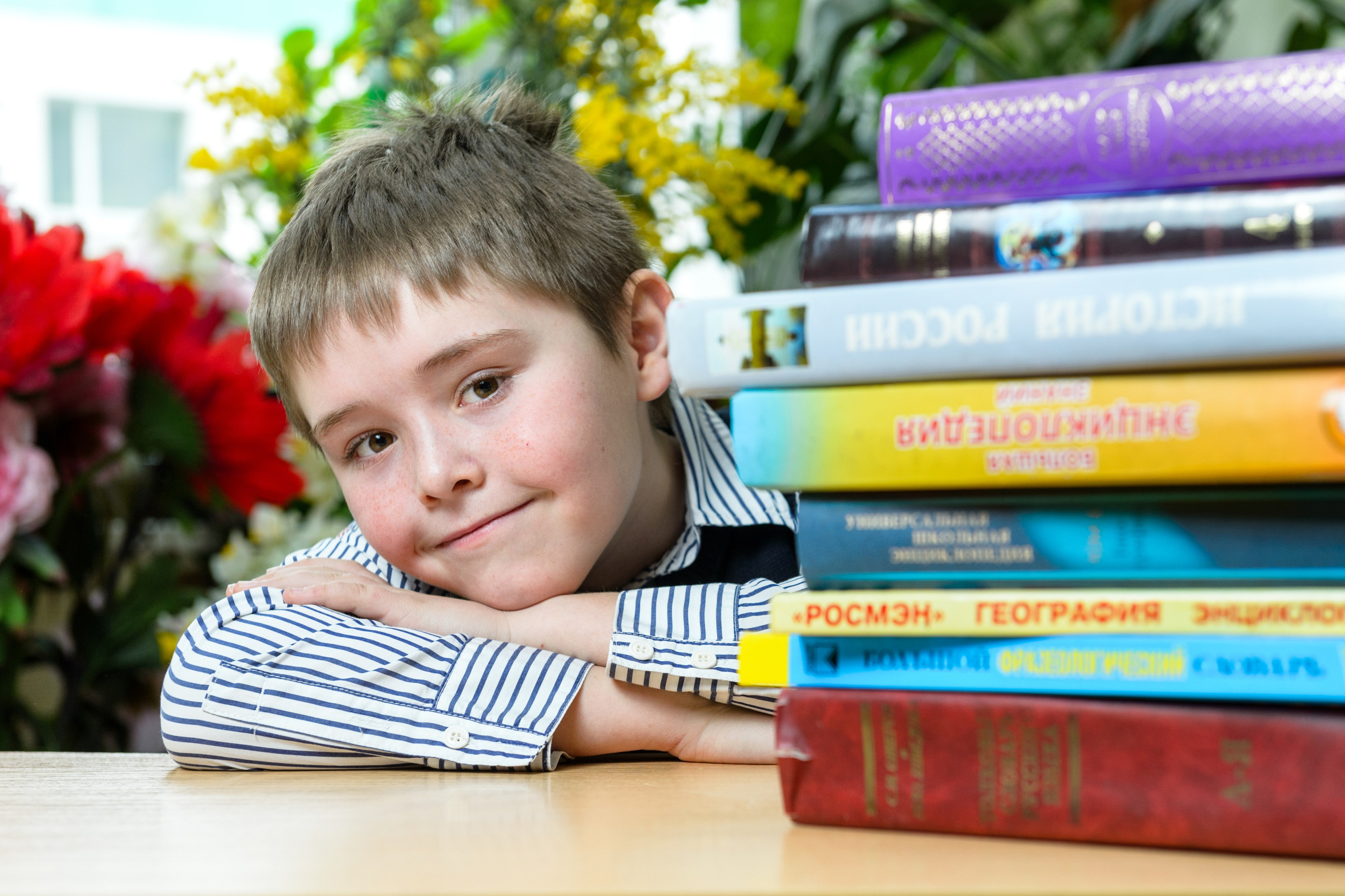 Школьник у стопки учебников в классе с цветами