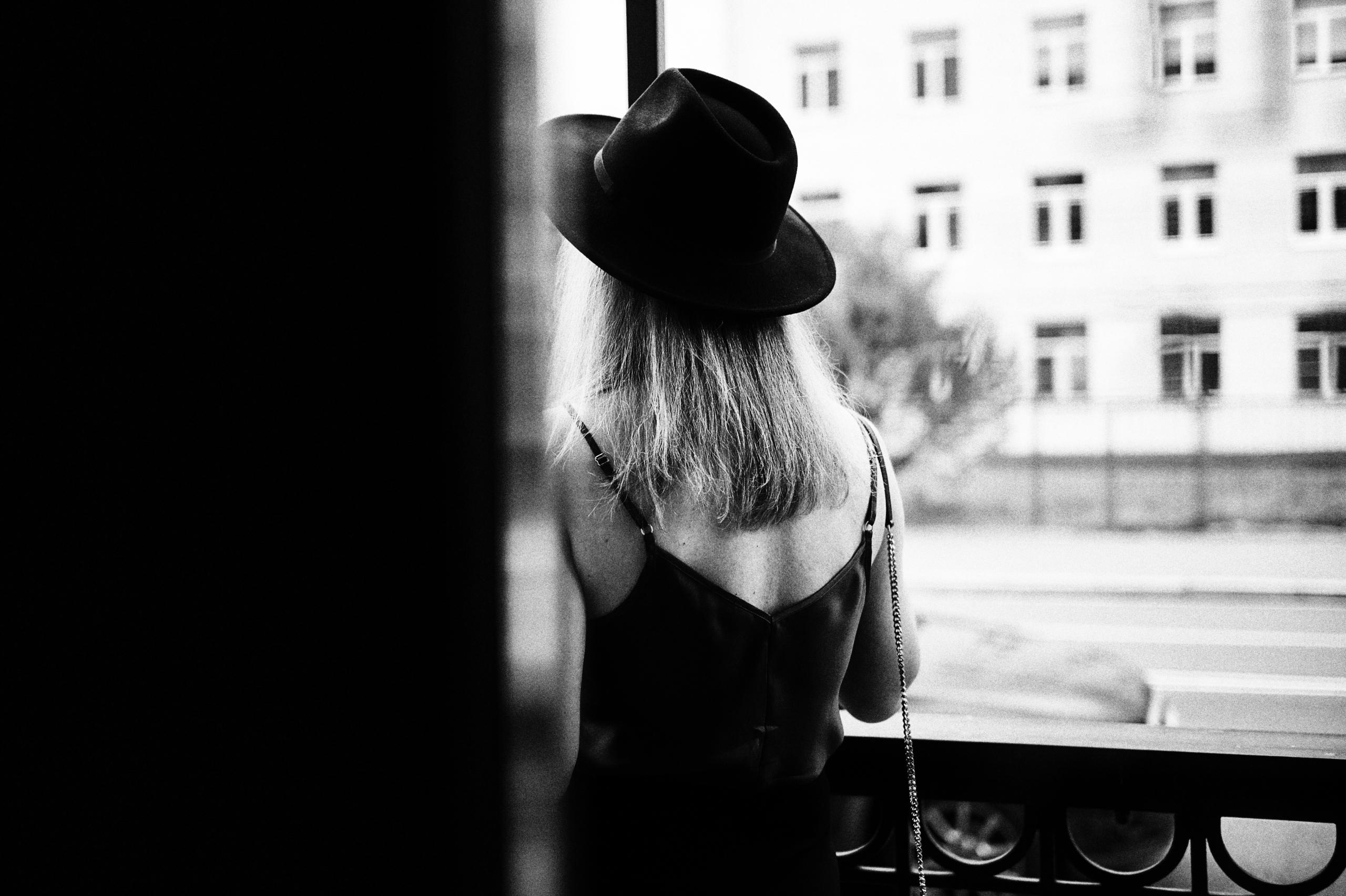 Девушка в шляпе стоит спиной на крыльце