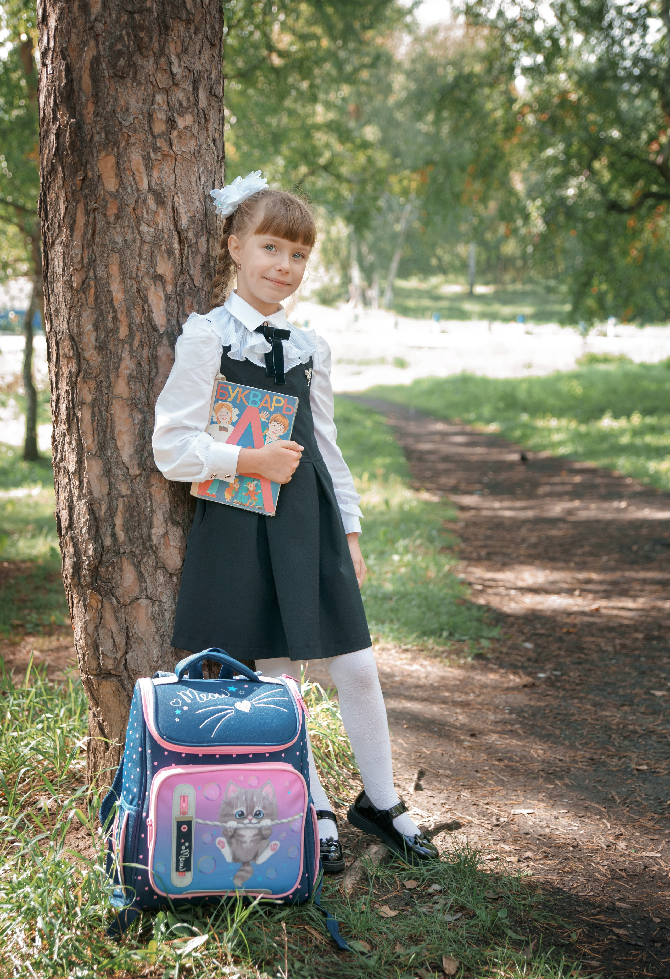 Детская фотосессия осенью - школьница стоя с учебником у дерева