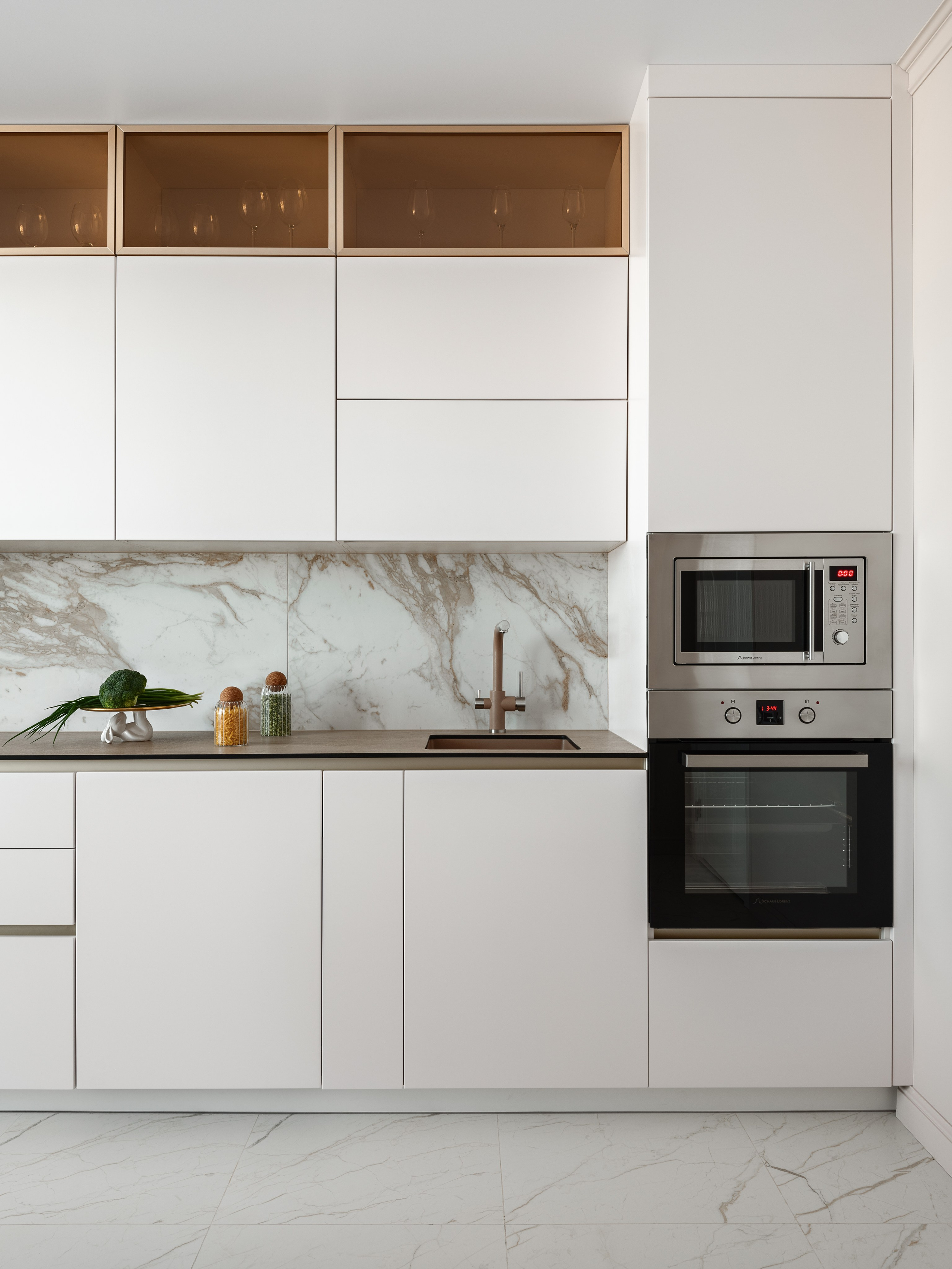 Минималистичная кухня с встраиваемой техникой, белыми шкафами, акцентом на мраморный фартук и теплое освещение; гармоничное сочетание светлого пола и стильного декора создано дизайнером Натальей Бунеевой, стилист Наталья Якушева, фотограф Сергей Денисенко.