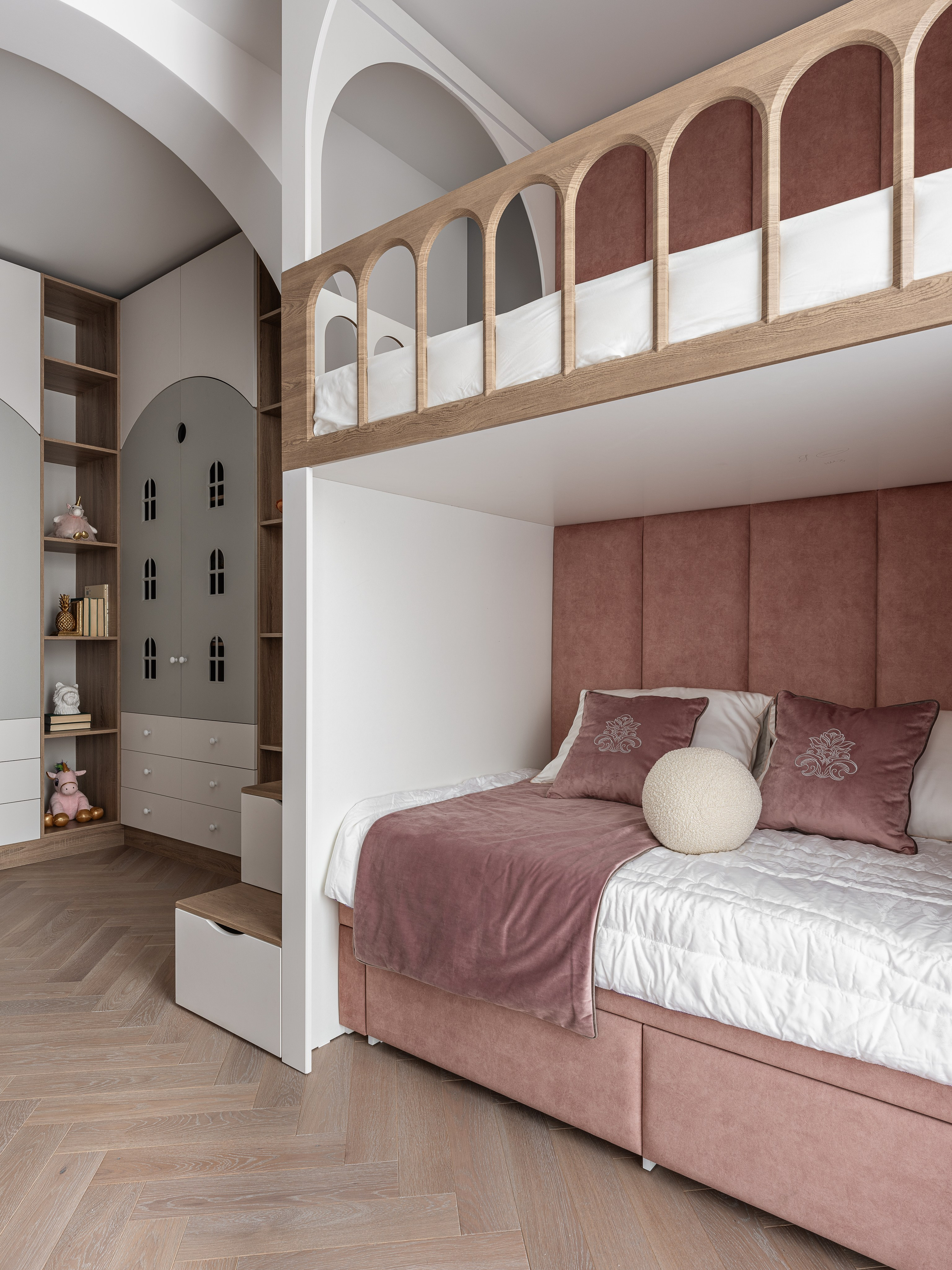 Интерьер детской комнаты с двухуровневой кроватью, мягким изголовьем пыльно-розового оттенка, лестницей с ящиками для хранения и встроенными шкафами в арочной нише, выполненный дизайнером Василиссой Бачевой, стилистом Натальей Якушевой и снятый Сергеем Денисенко.