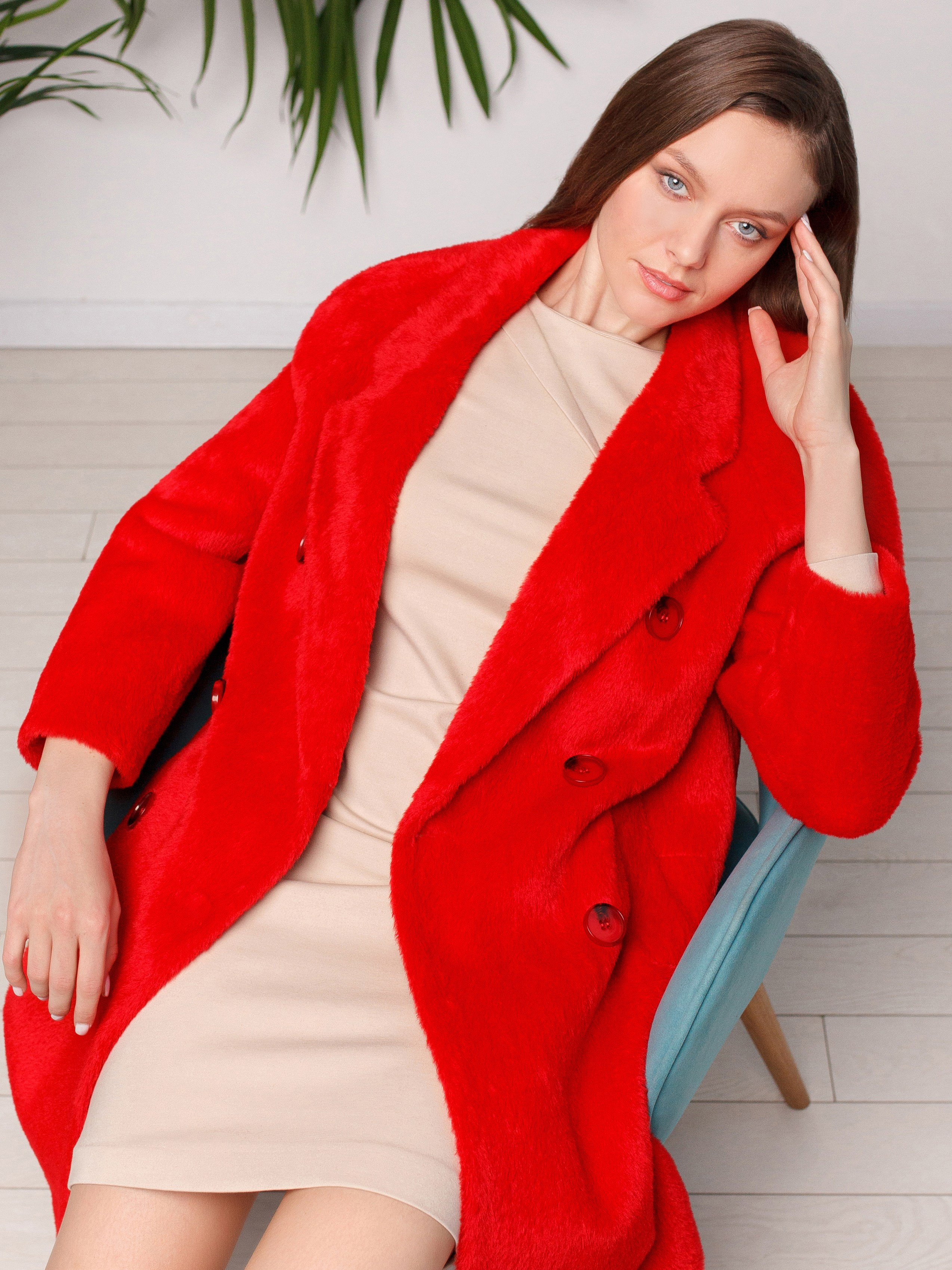 Девушка сидит на кресле в красном пальто и смотрит в камеру