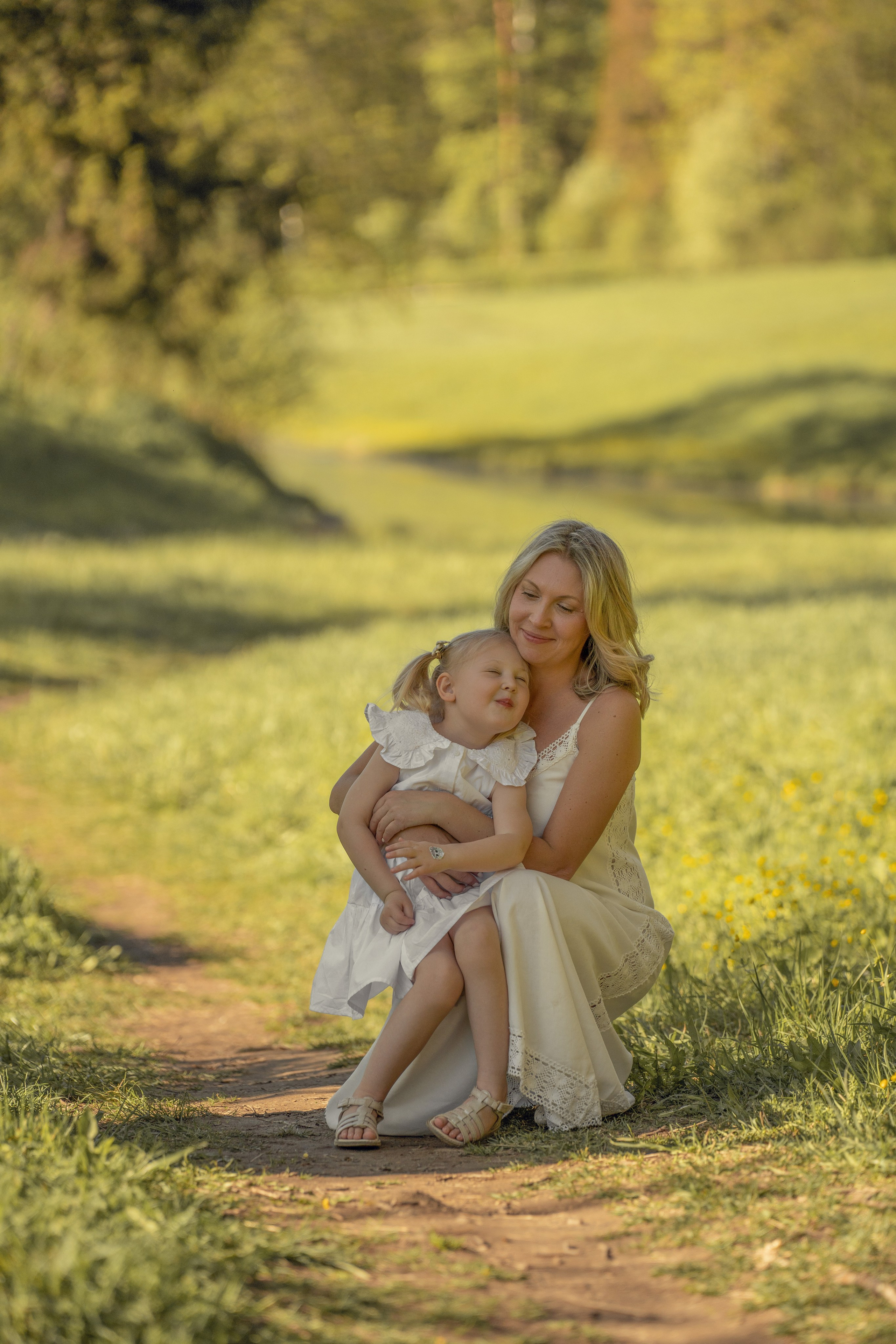 Мама обнимает свою дочку на прогулке в парке летом.