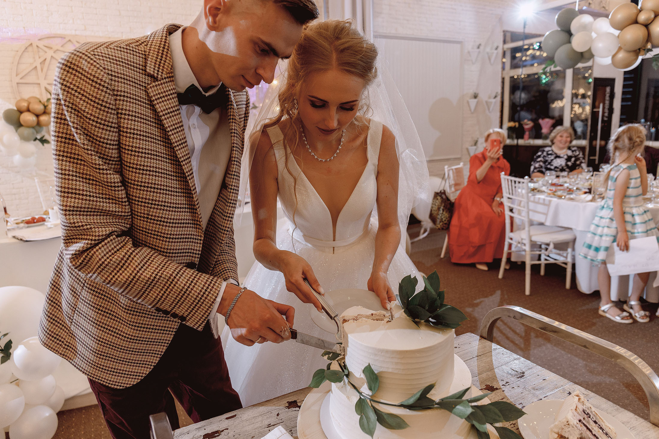 молодые режут свадебный торт на банкете
