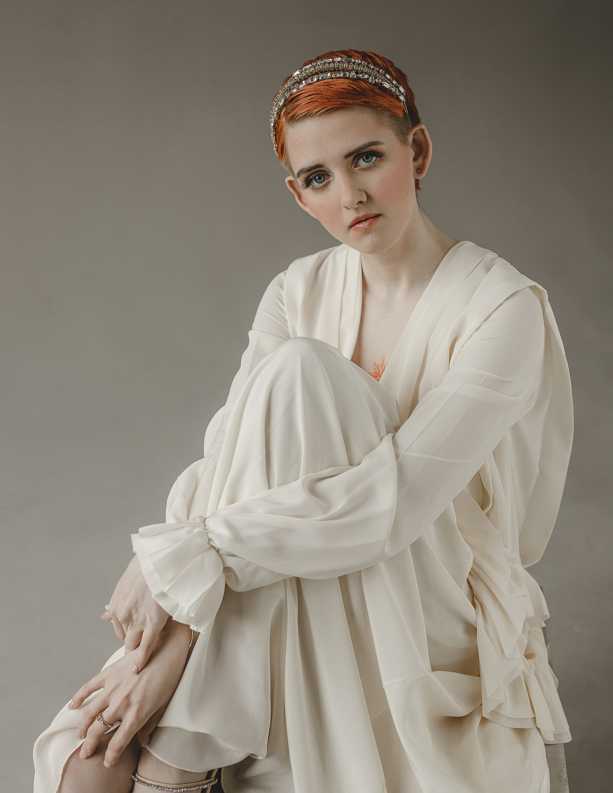 Рыжая девушка в летящем белом платье Виктории Бэкхем в студии сидит на кубе