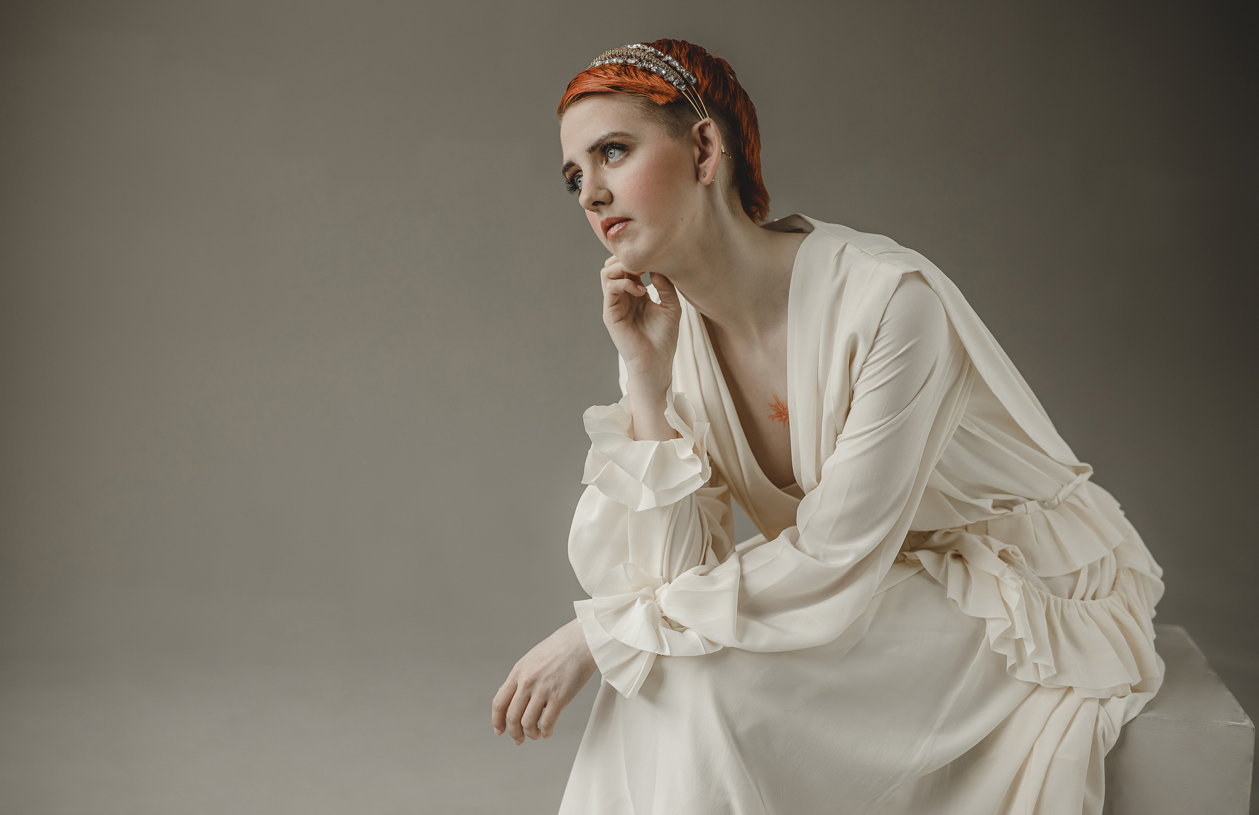 Рыжая девушка задумчивая с рыжей татуировкой в белом платье Виктории Бэкхем в студии 